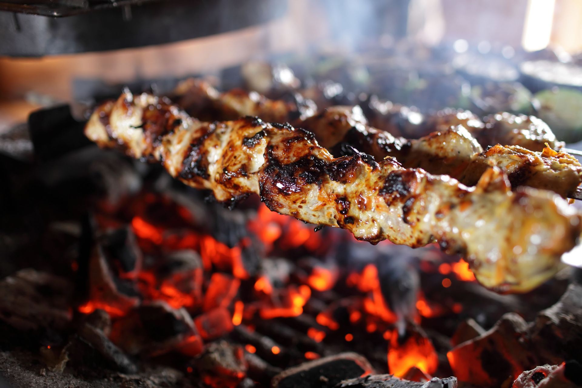 Skewered meat grilling over glowing coals, with charred edges and smoke rising