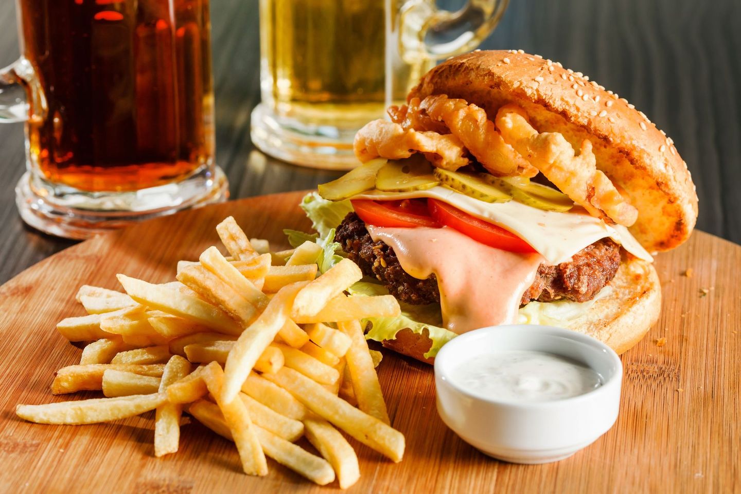Burger, fries, and dipping sauce on a wooden table with drinks in the background