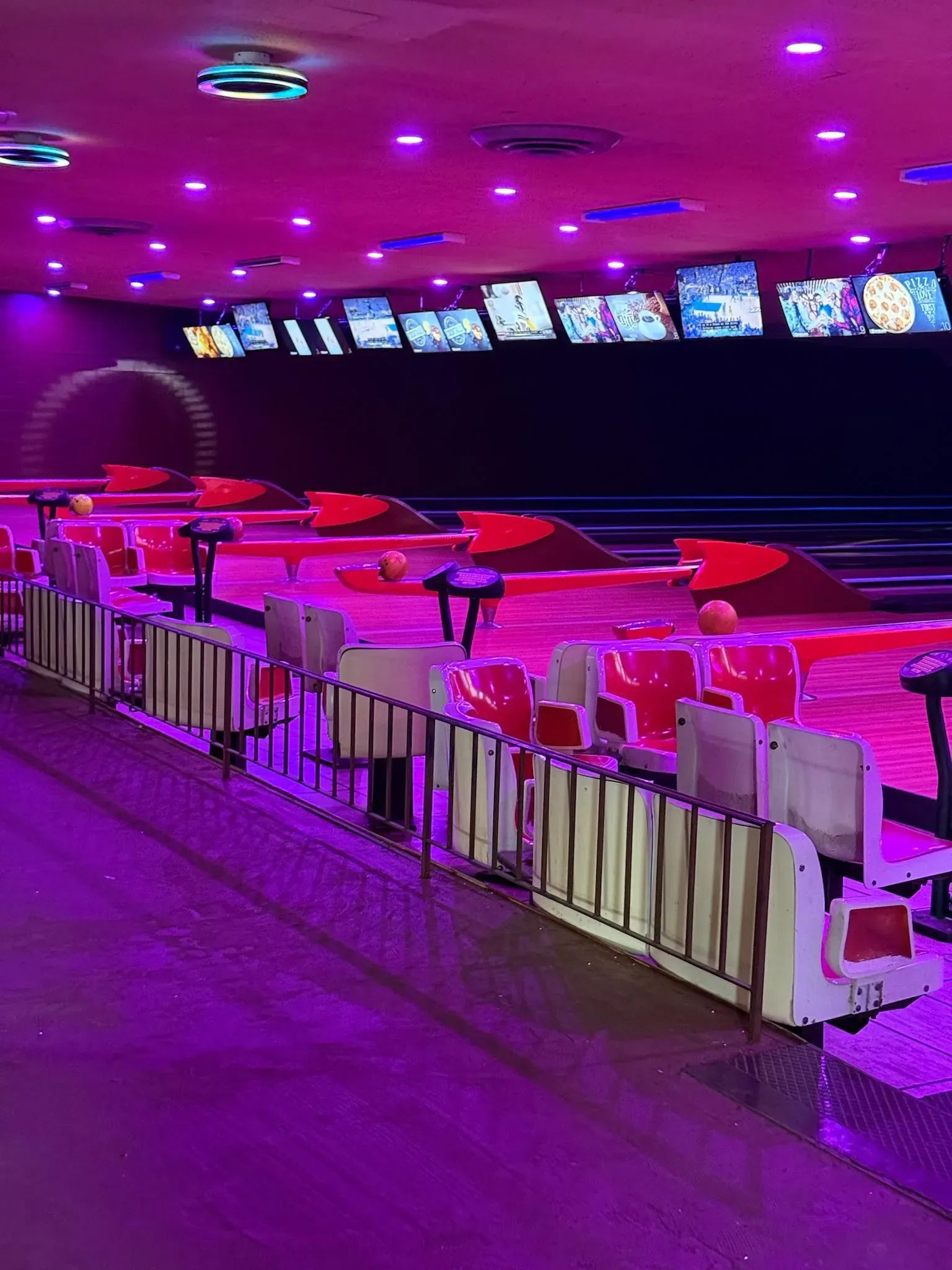 Neon-lit bowling alley with lanes, seating, and overhead monitors