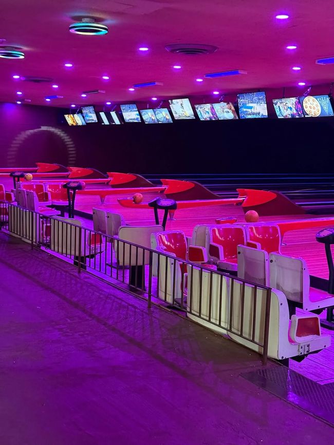 Neon-lit bowling alley with lanes, seating, and overhead monitors
