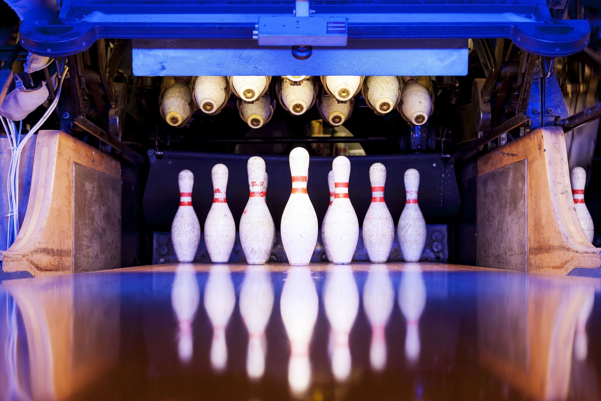 Bowling alley pins lined up under the pinsetter, with their reflections on the polished lane.