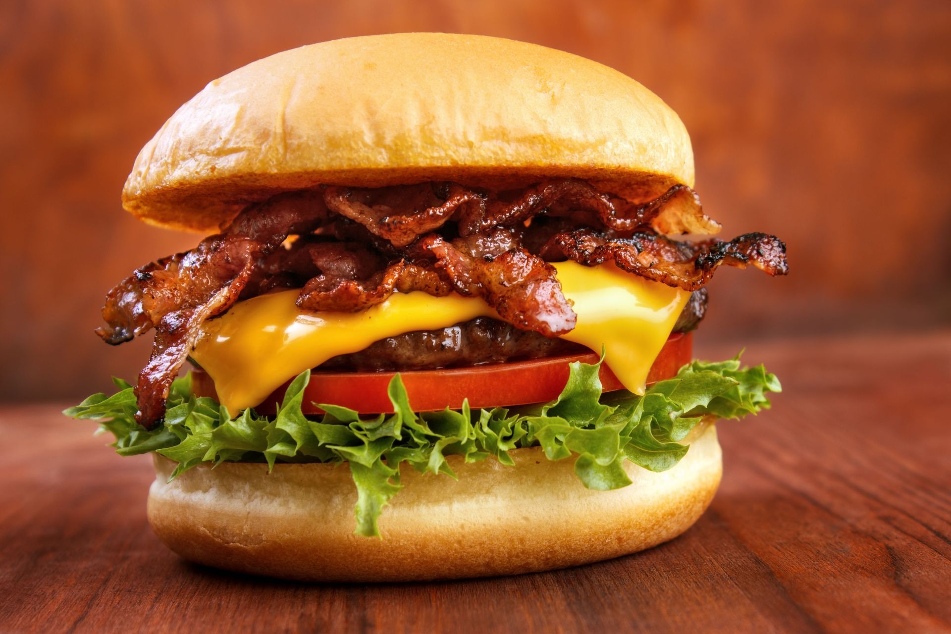 Bacon cheeseburger with lettuce, tomato, and melted cheese on a bun against a wooden background