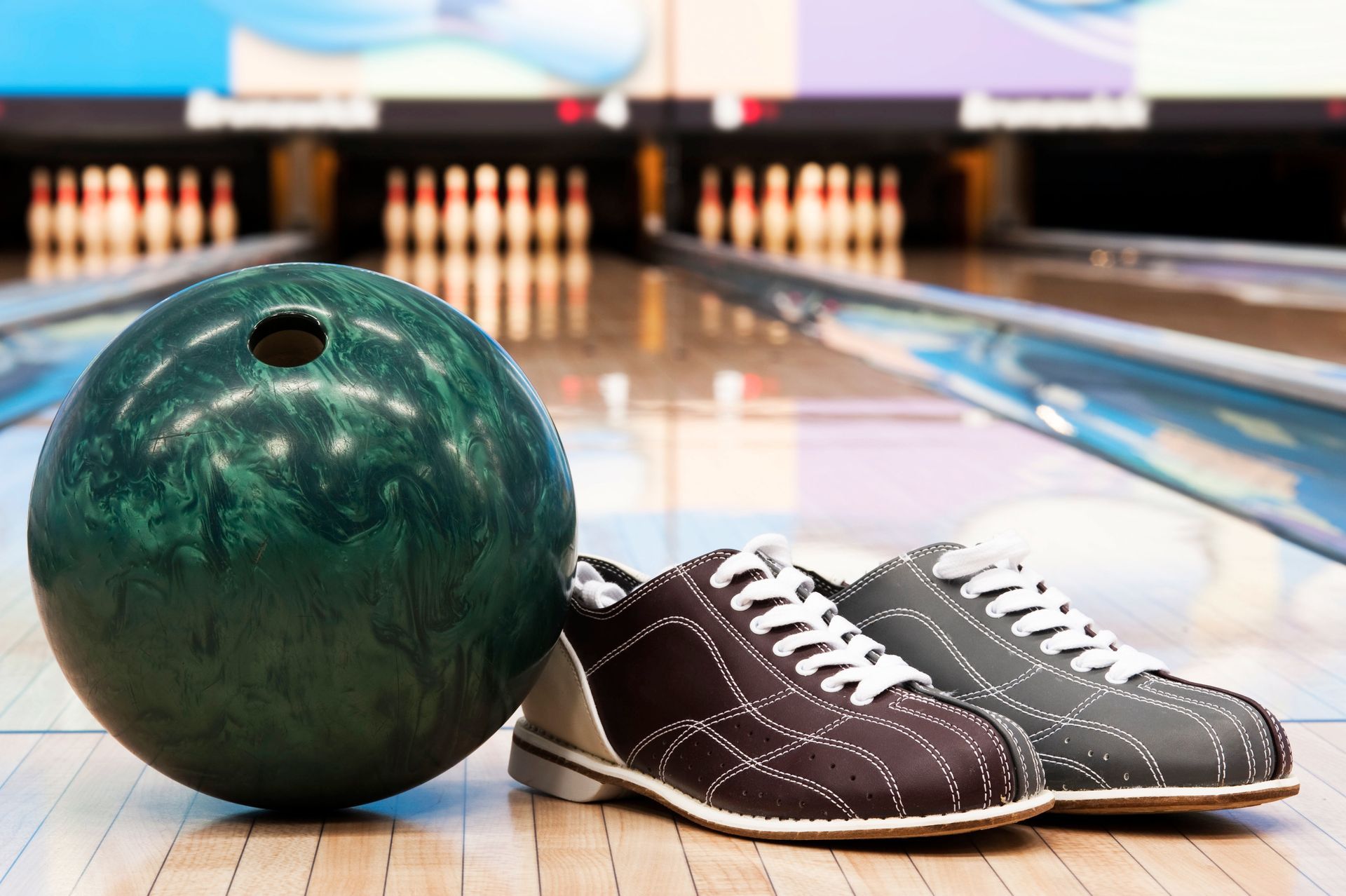 Bowling ball and pair of shoes on a lane, with pins in the background