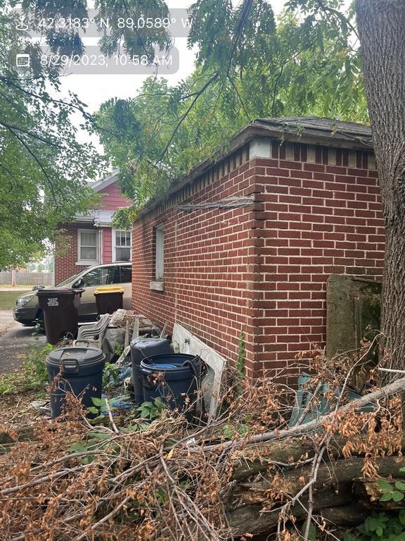 Red brick building with a small window, garbage bins, and debris in a yard.