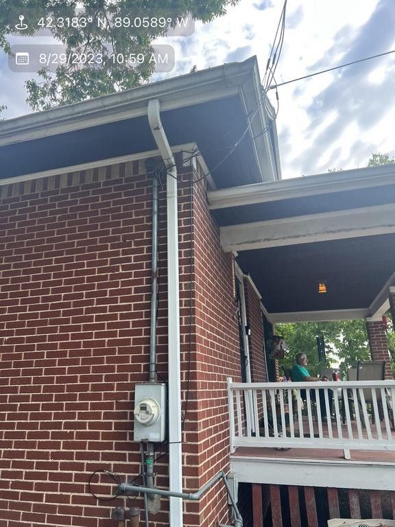 Brick building exterior with porch and gutters; person on porch. Electrical meter on side.