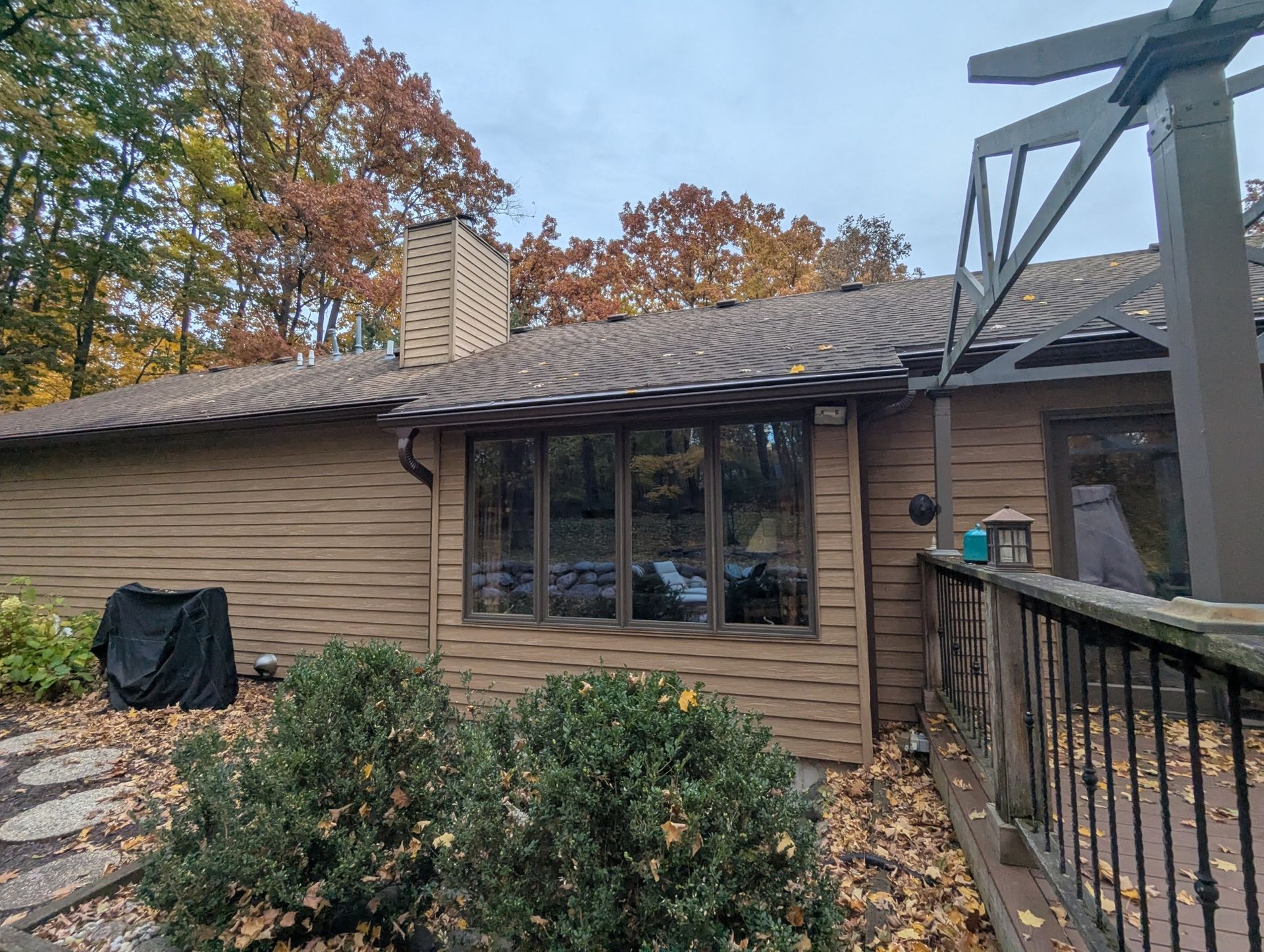 Brown house exterior with dark roof, windows, and deck, surrounded by fall foliage.