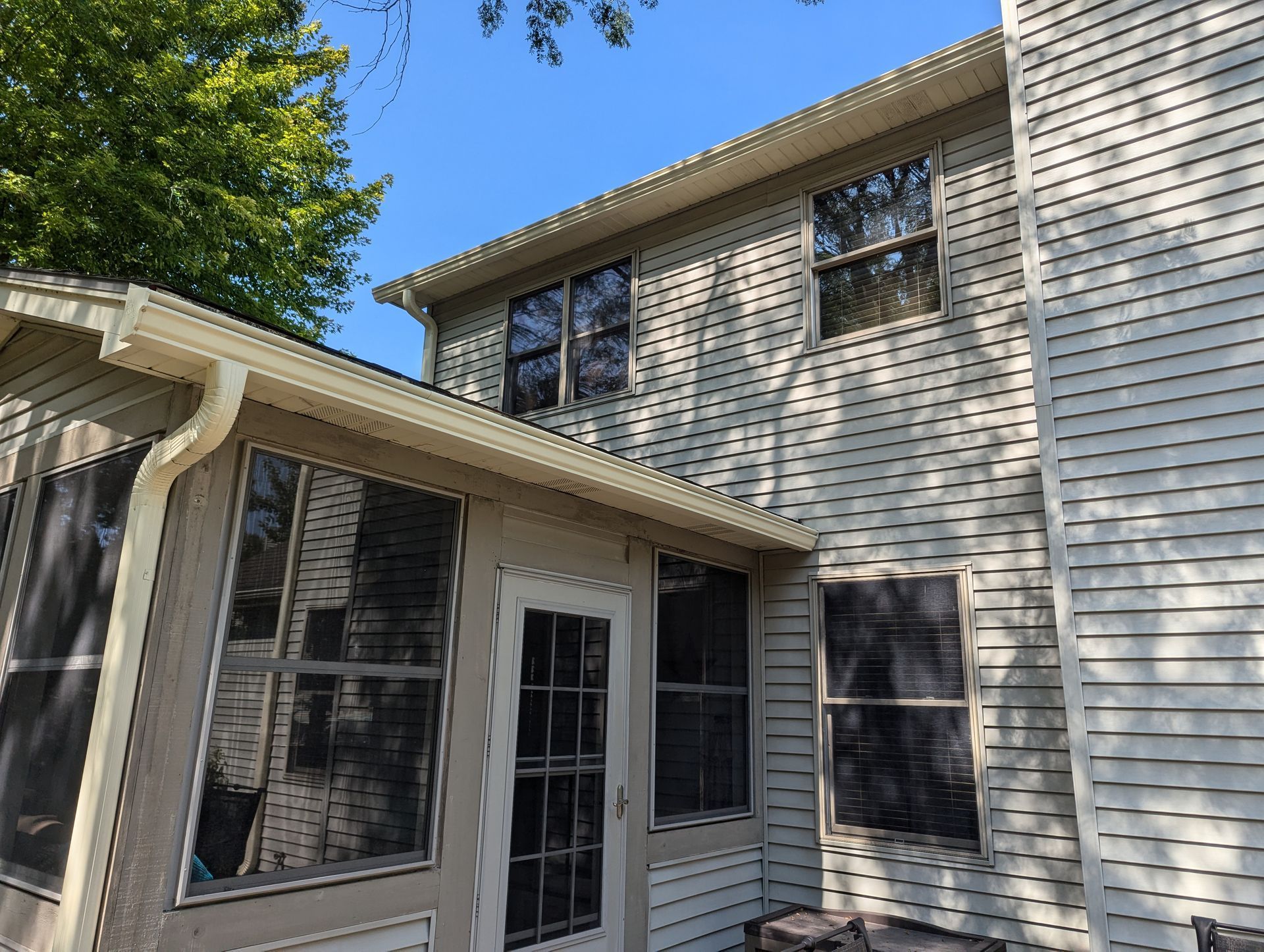 Exterior of a two-story house with a sunroom, beige siding, and windows; a blue sky.