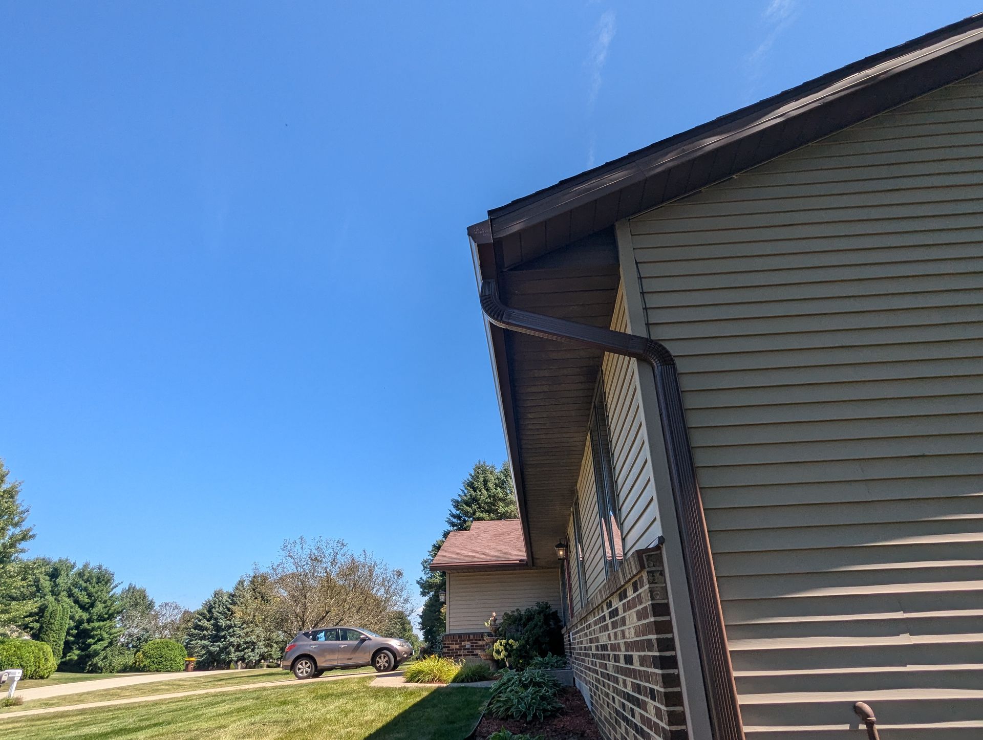 Corner of a house with brown trim and gutters, green siding, and a blue sky.