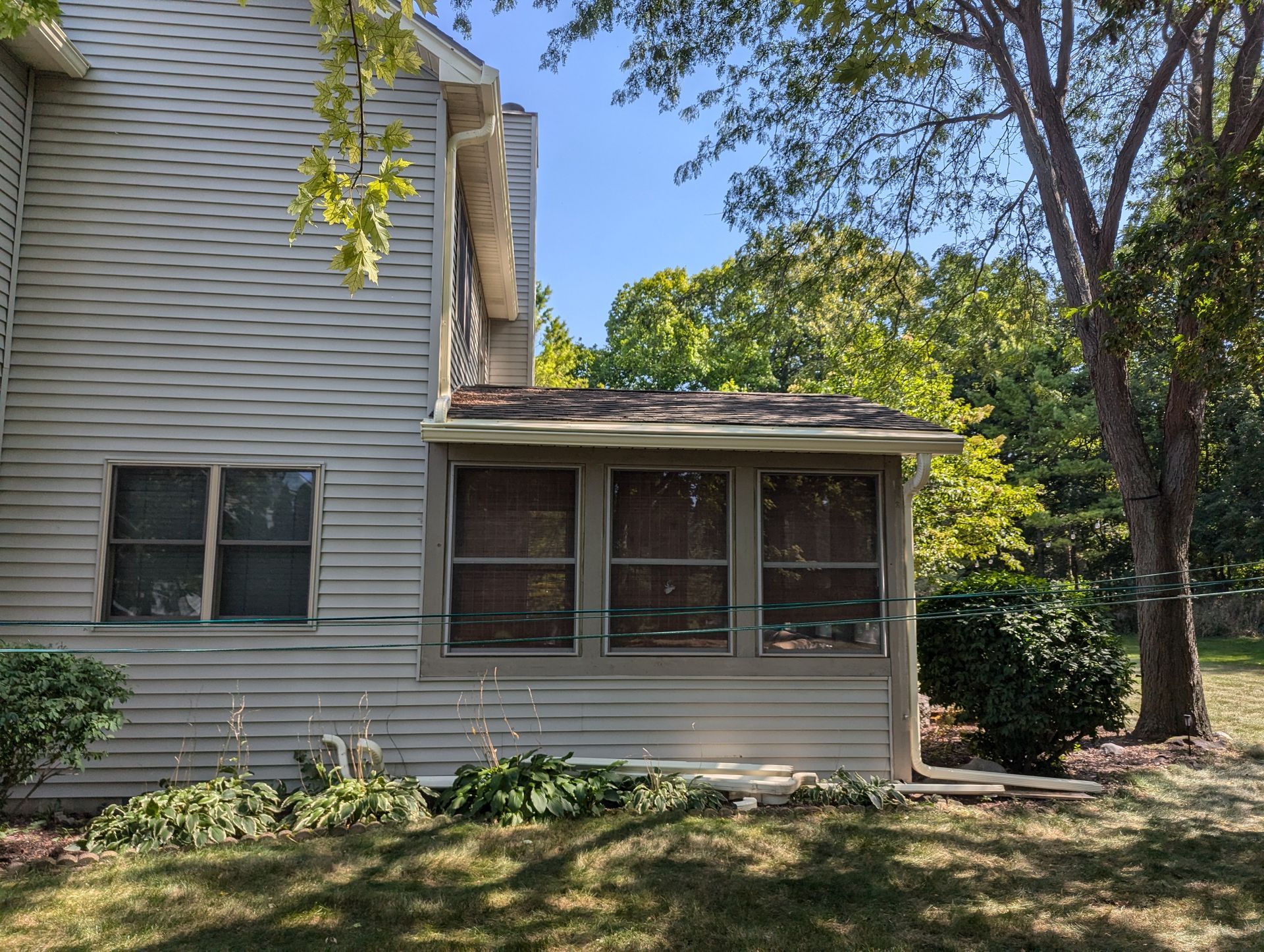 A light-colored house with a screened porch under a sunny sky, surrounded by trees and grass.