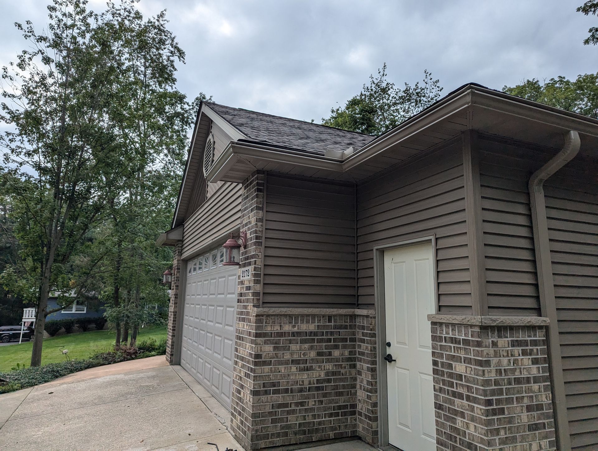 Garage with gray door, brown siding, brick accents, and a sloped roof under an overcast sky.