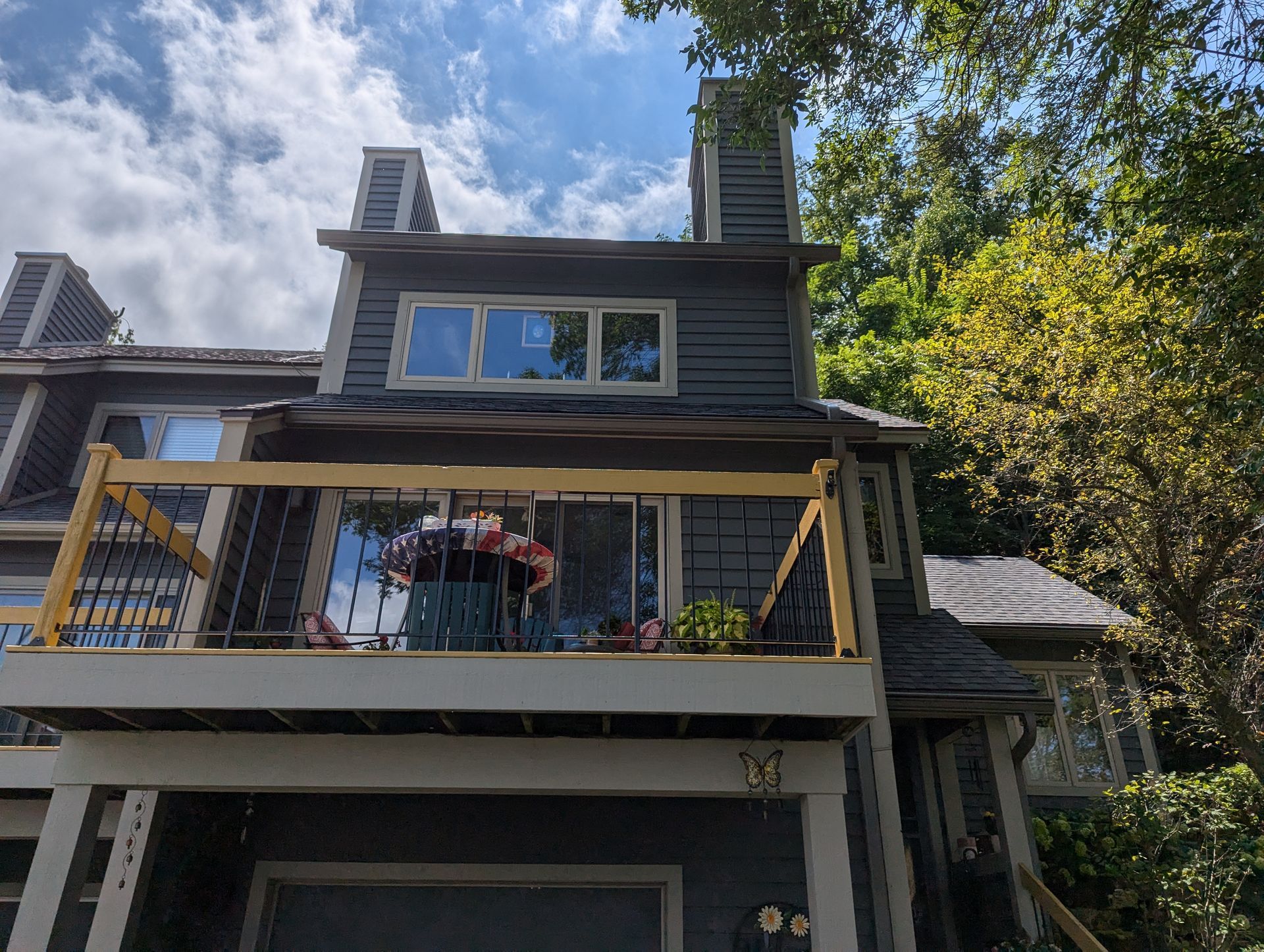 Two-story house with balcony, gray siding, and a partially cloudy sky.