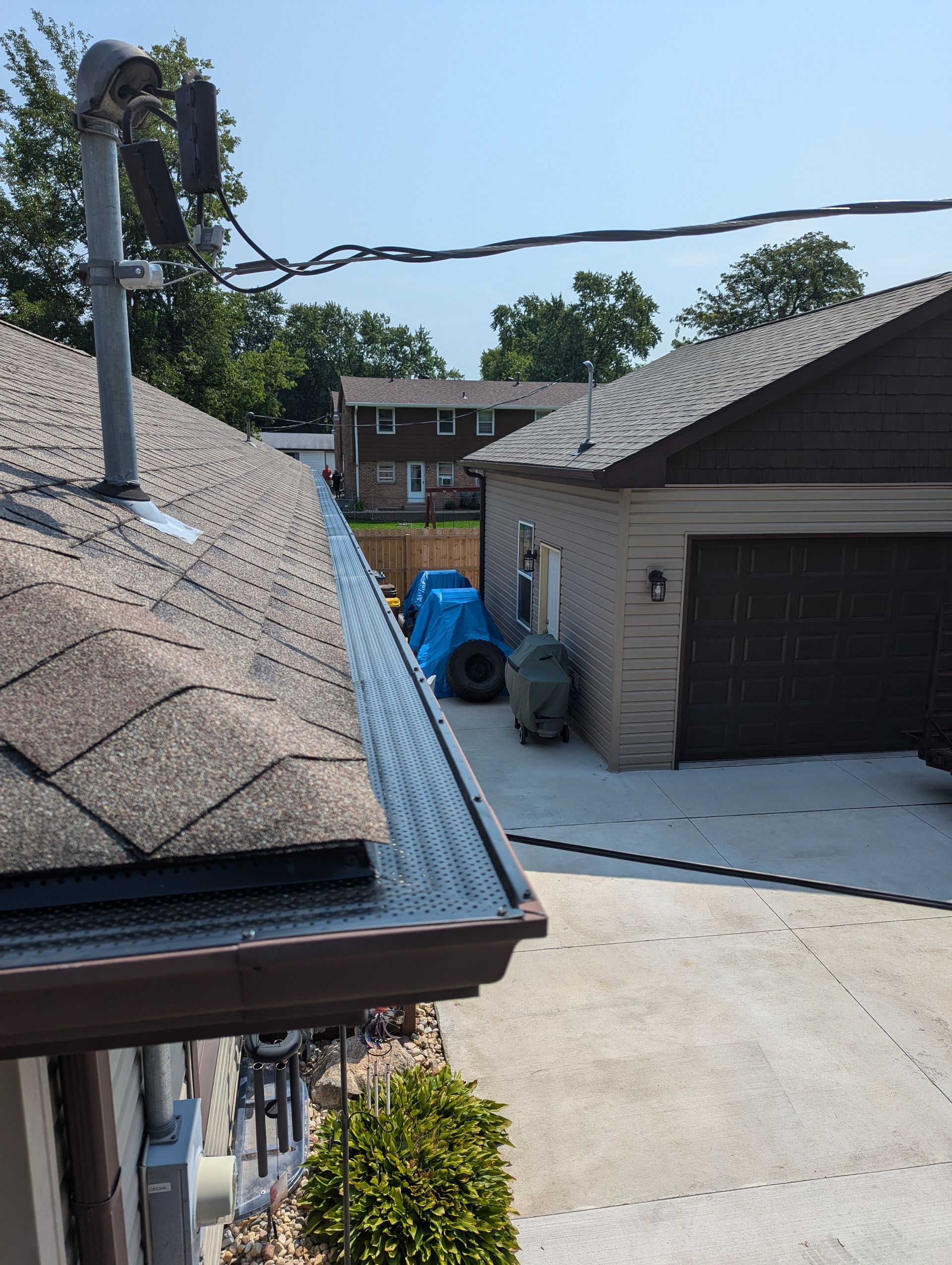 View of rooftops, a garage, and a driveway on a sunny day. Power lines and a small green bush are also present.