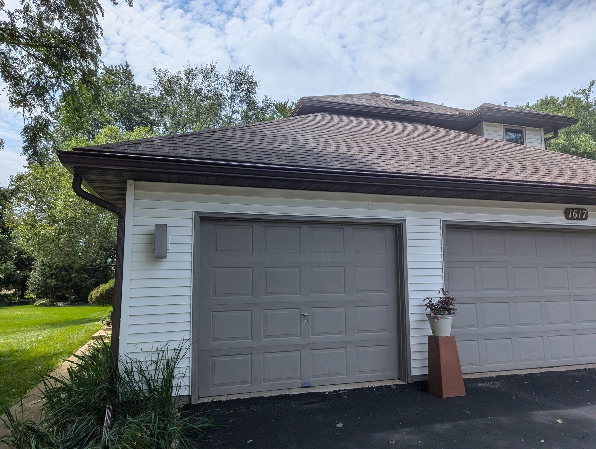 Garage with two gray doors and a brown roof against a cloudy sky.