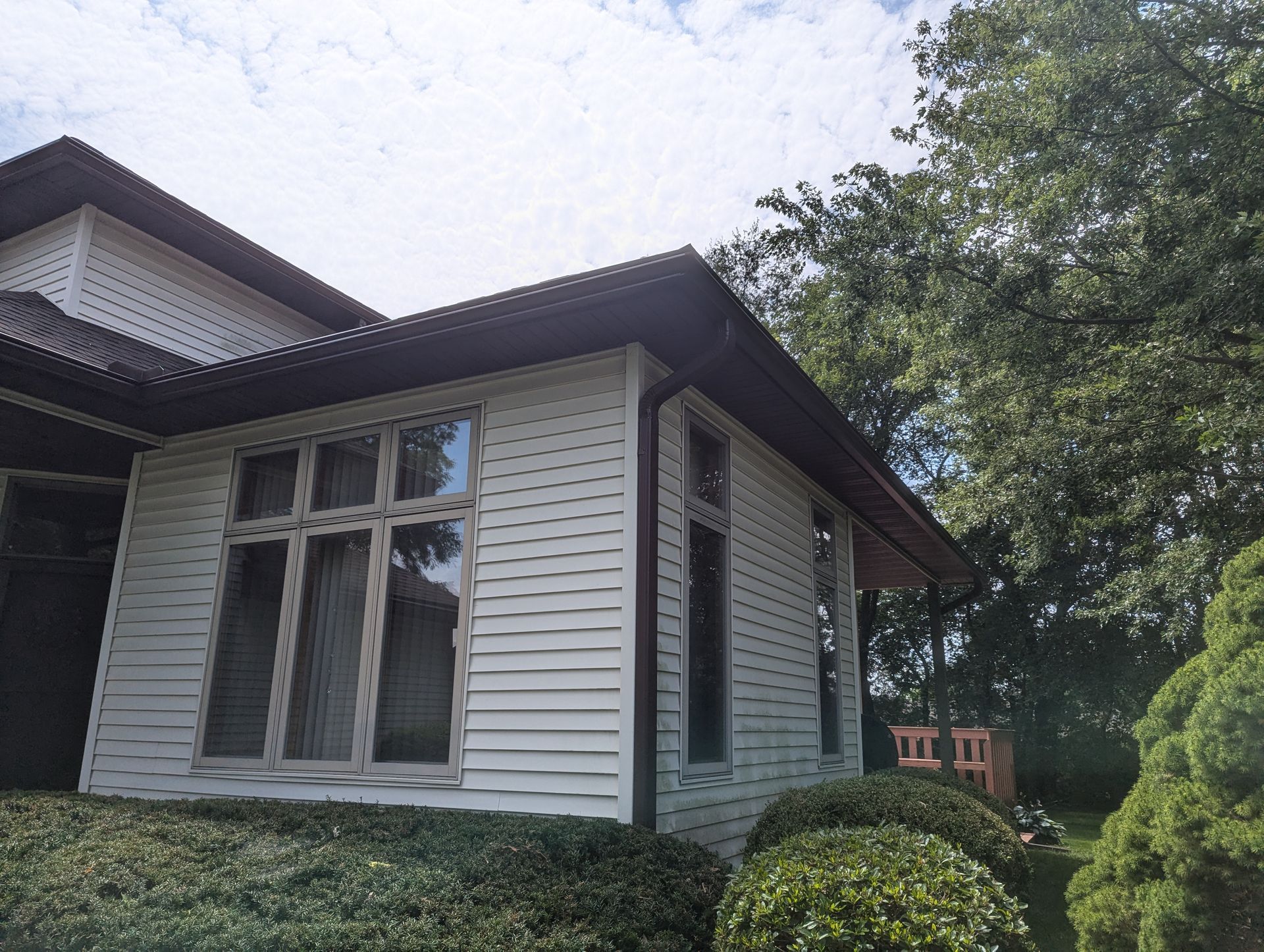 White house with dark roof and windows, next to green bushes and trees.