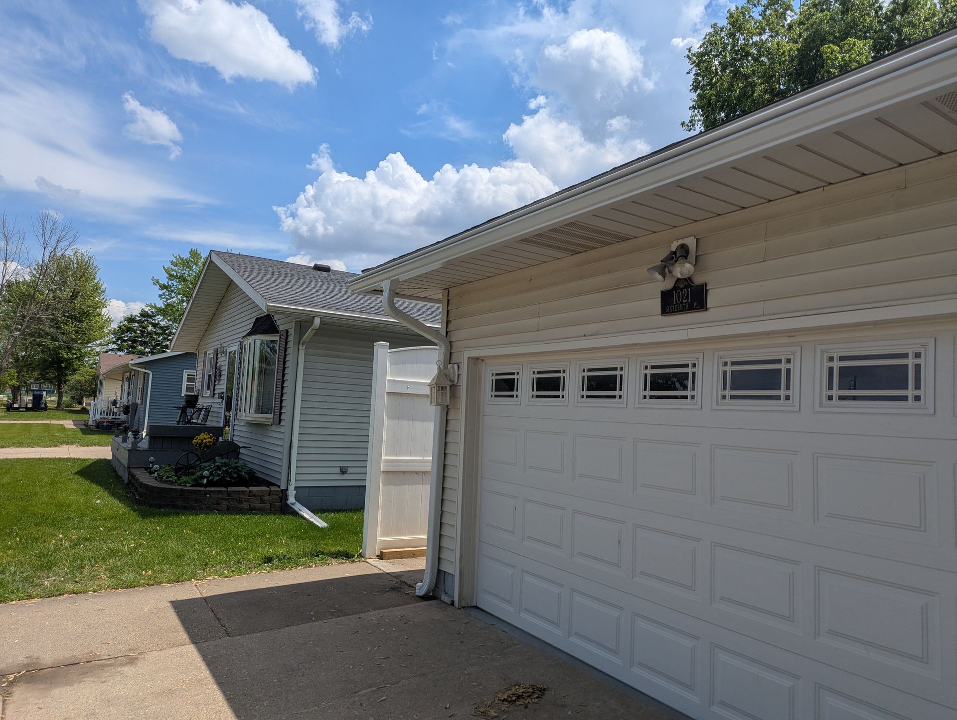 Exterior of a house and attached garage on a sunny day. Beige siding, white garage door, and blue sky.