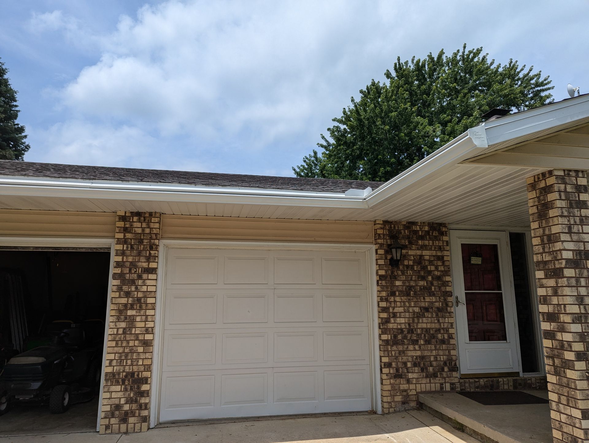Two-car garage with white door and brick facade, front door to the right. Overcast sky.