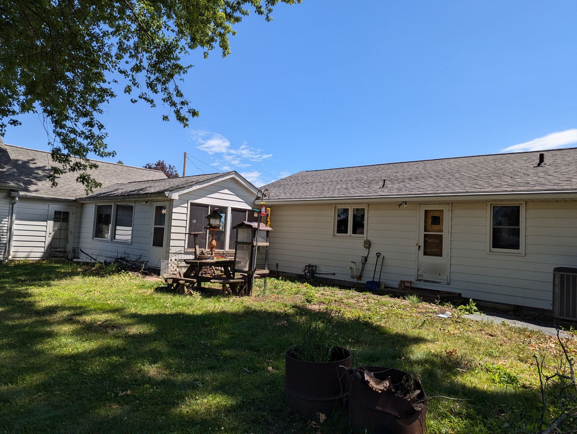 Backyard with two aging, white houses, grassy yard, blue sky.