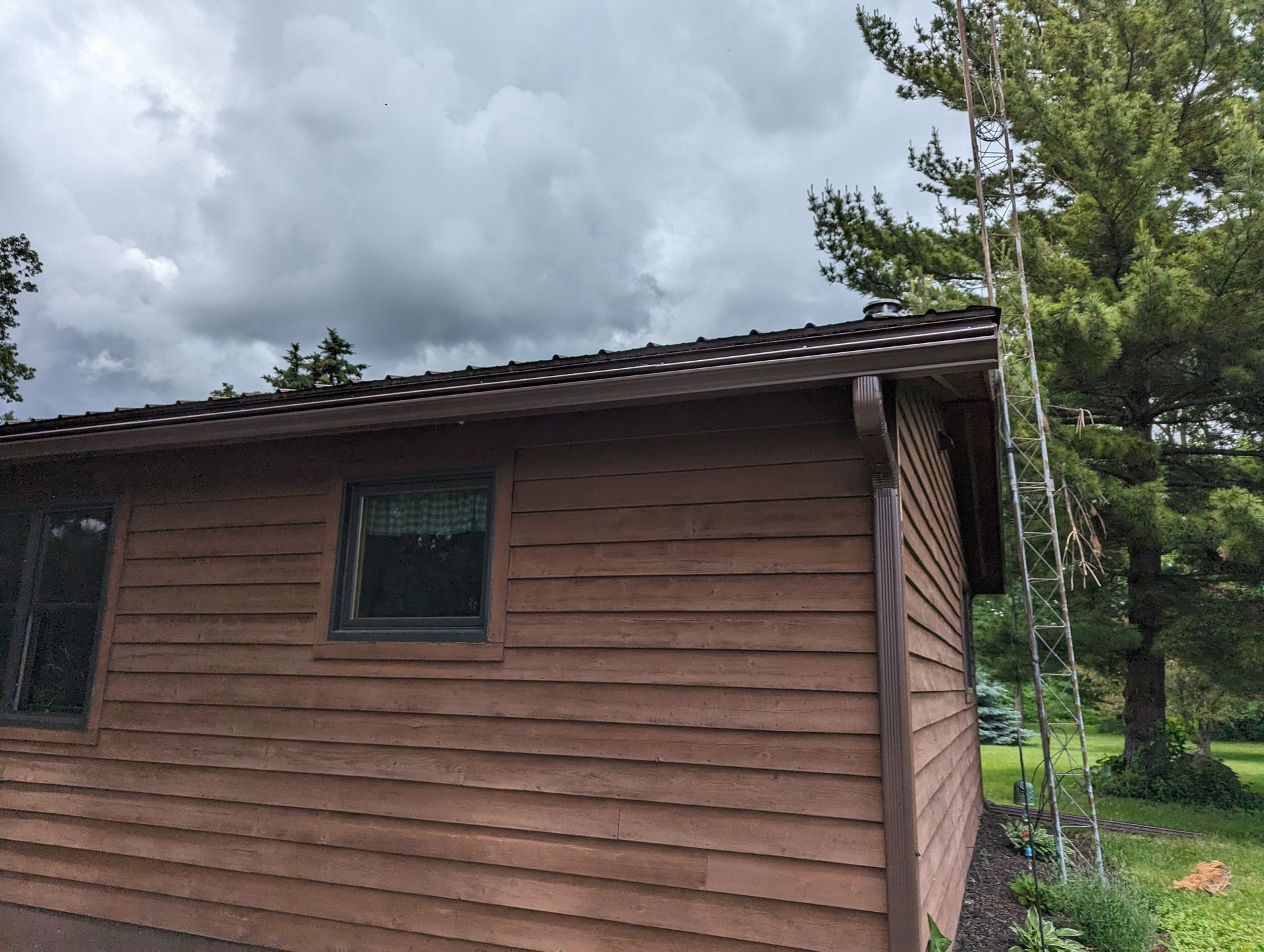 Brown building with a dark roof and a tall metal structure, set against a cloudy sky.