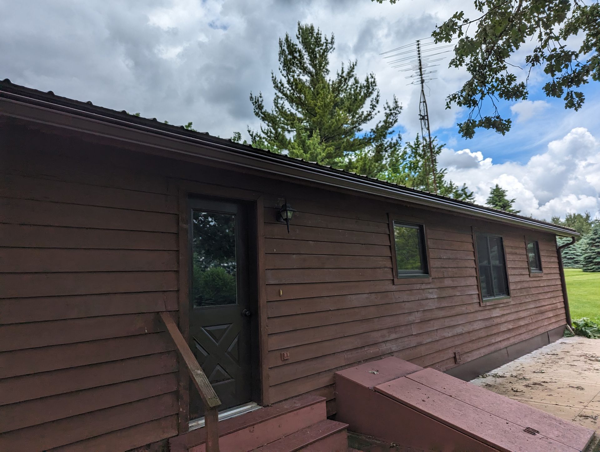Brown house exterior with a door, windows, and steps, against a cloudy sky.