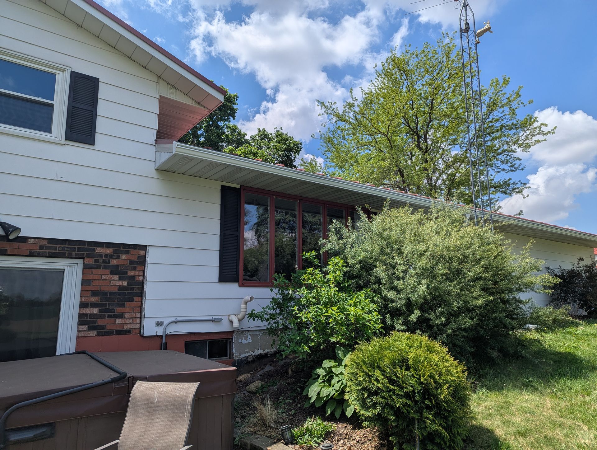 White house with red-trimmed windows and a bush in front, under a partly cloudy sky.