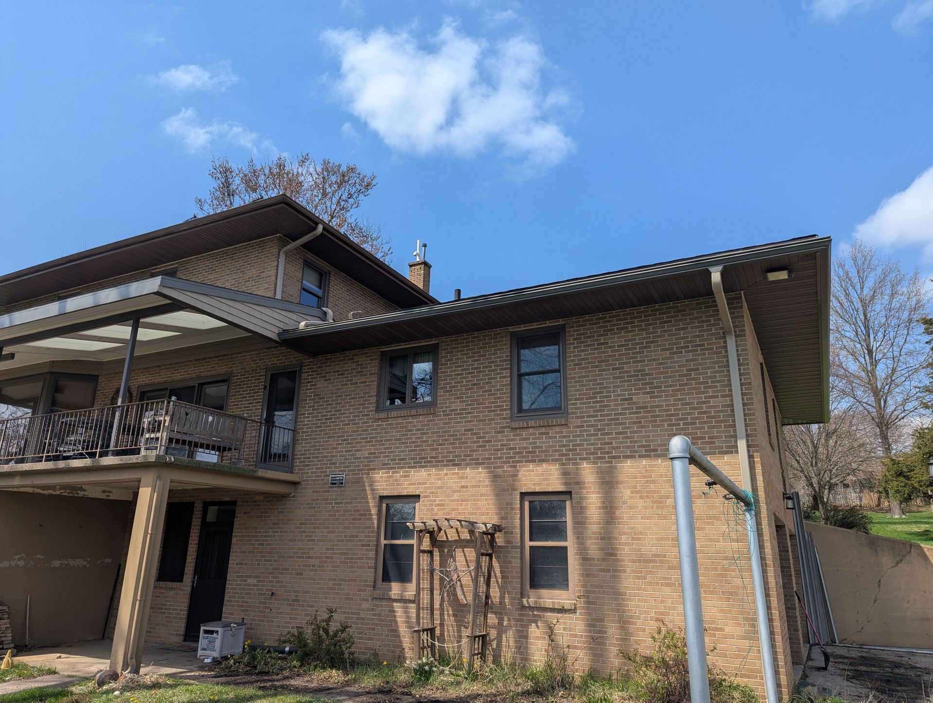 Two-story brick house with brown trim and balcony under a blue sky with clouds.