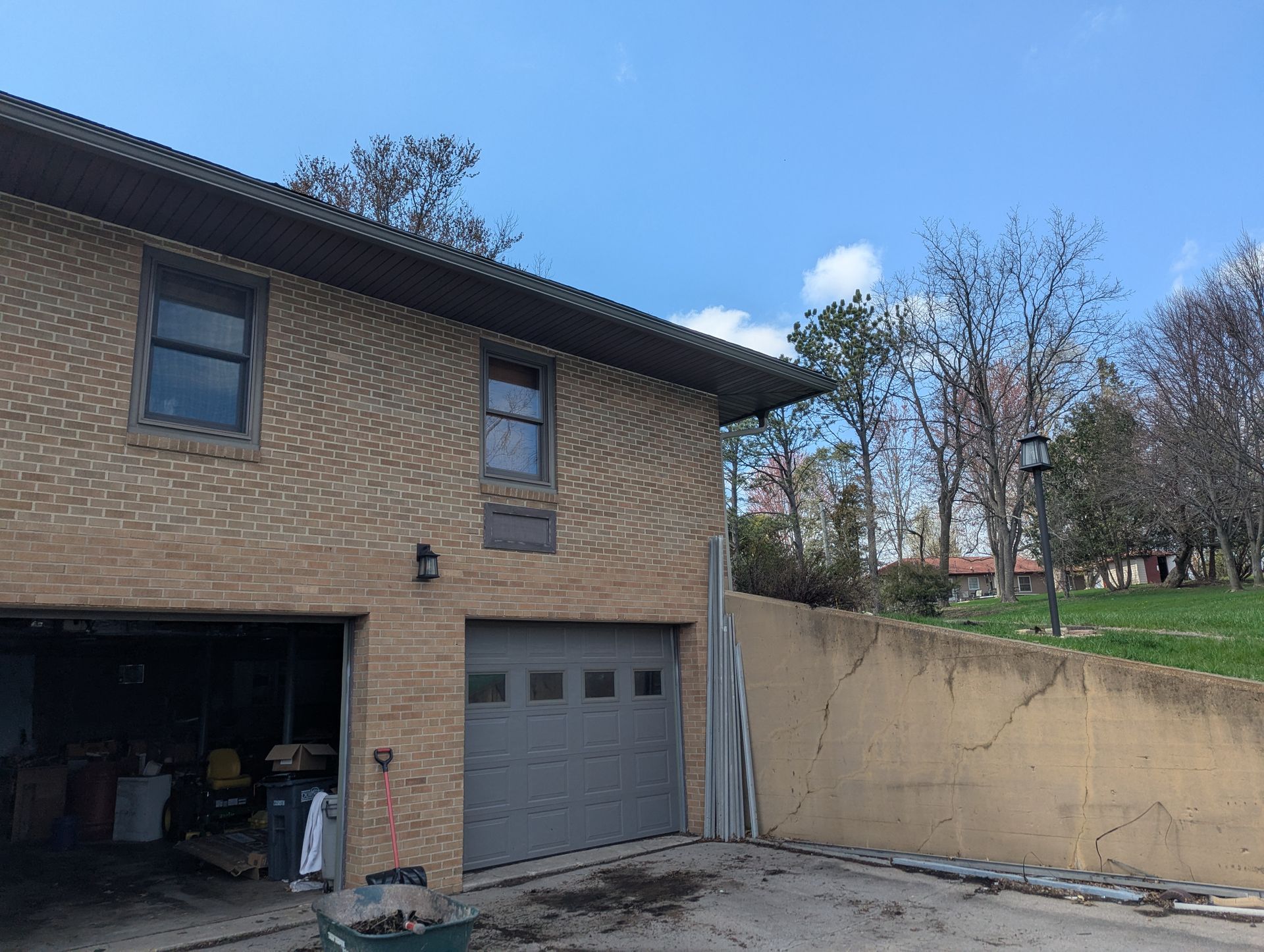 Tan brick house with two garage doors and a sloping retaining wall under a blue sky.