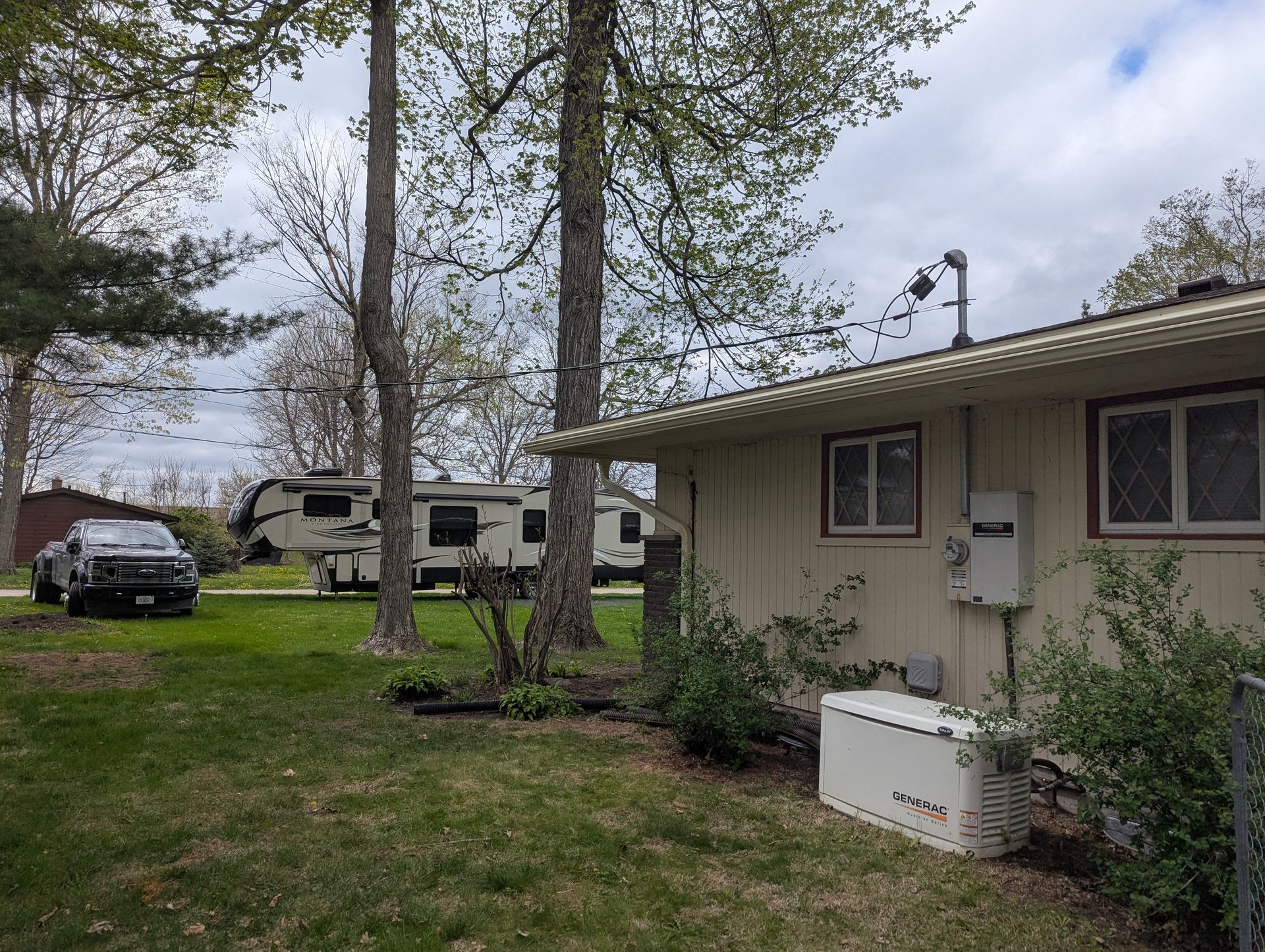 Backyard view with RVs, a house, a vehicle, trees, and cloudy sky.