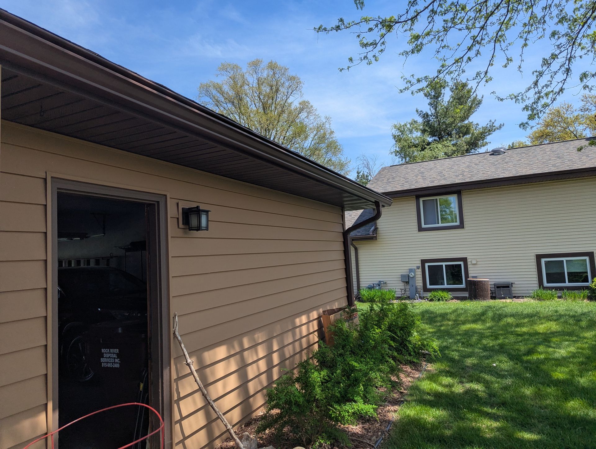 Beige-sided house with a garage, brown trim, and green lawn on a sunny day.