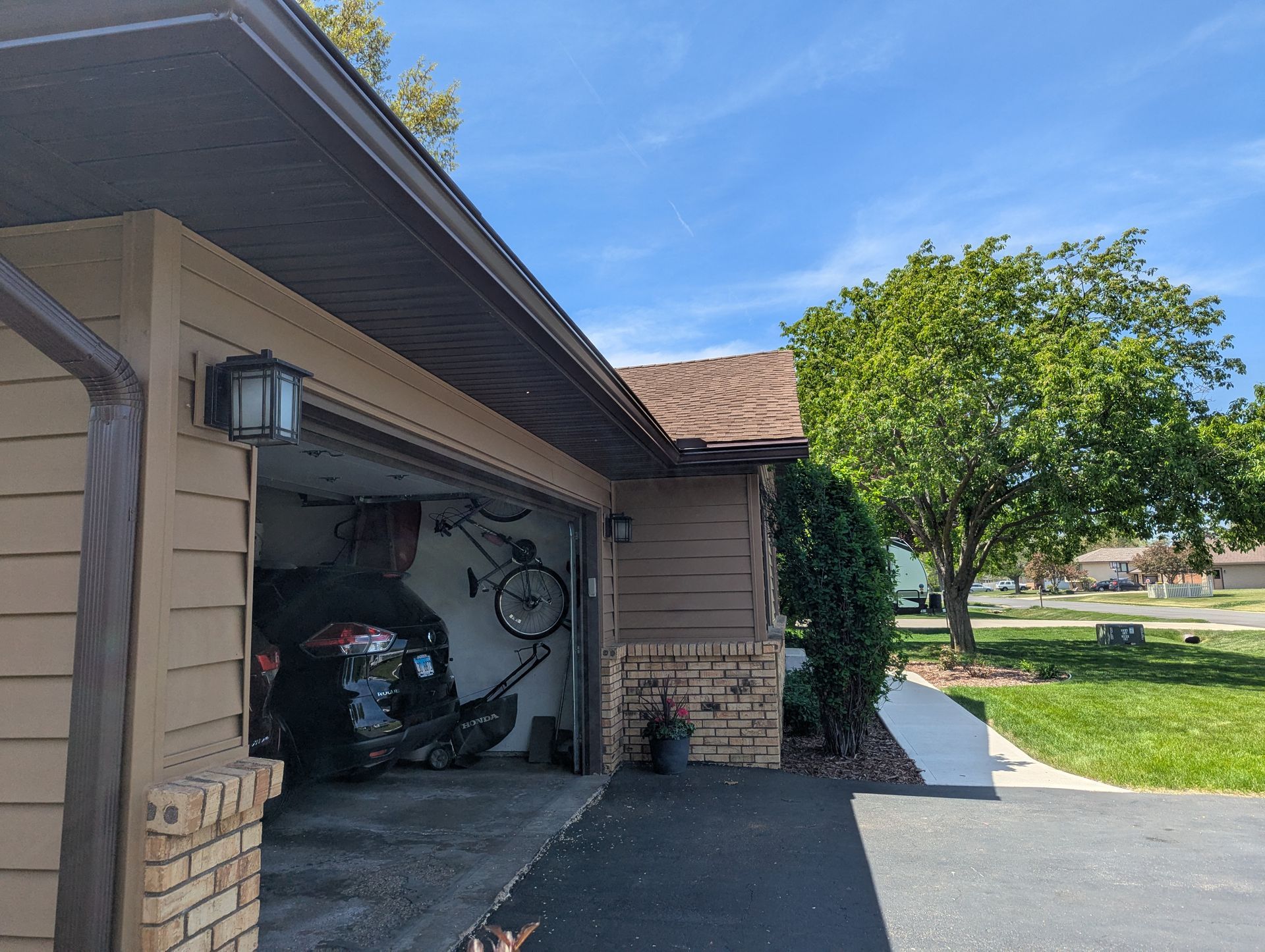 Garage with open door, vehicle, bicycle, and tree in a sunny setting with a blue sky.