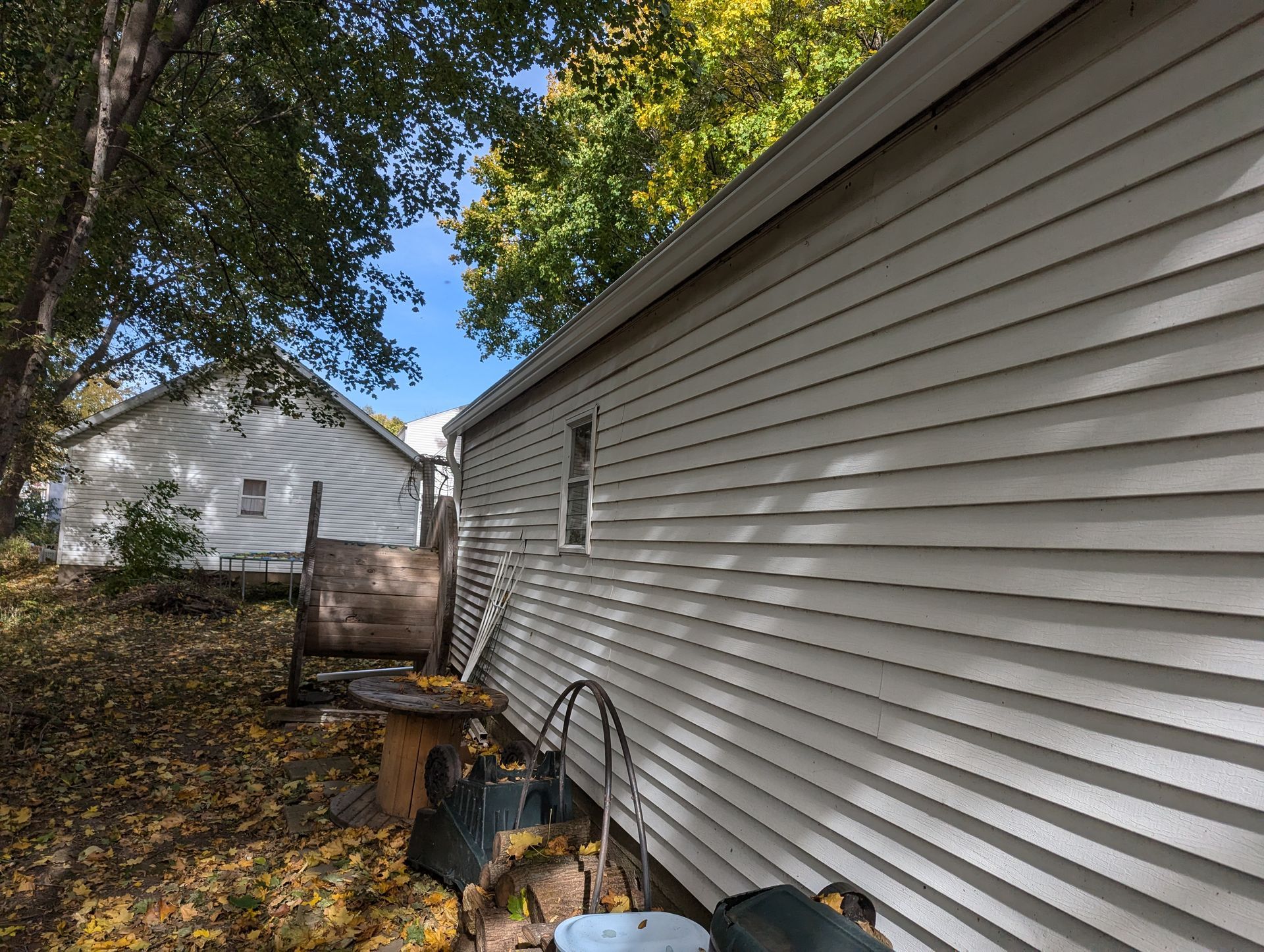 White clapboard siding on a building with a window; another building in the distance with fall foliage.