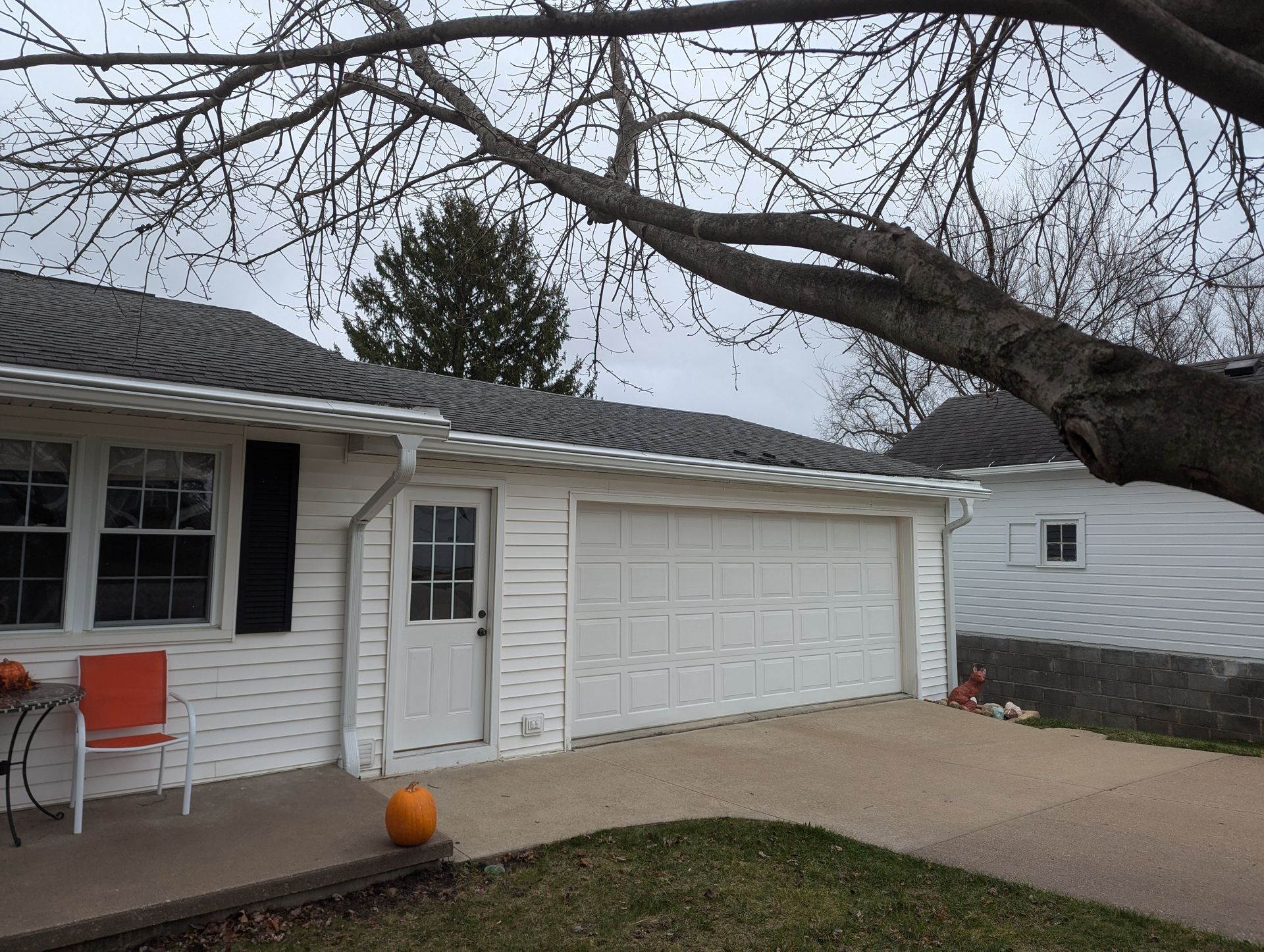 White house with attached garage, orange chair, and pumpkin in front. Overcast day.