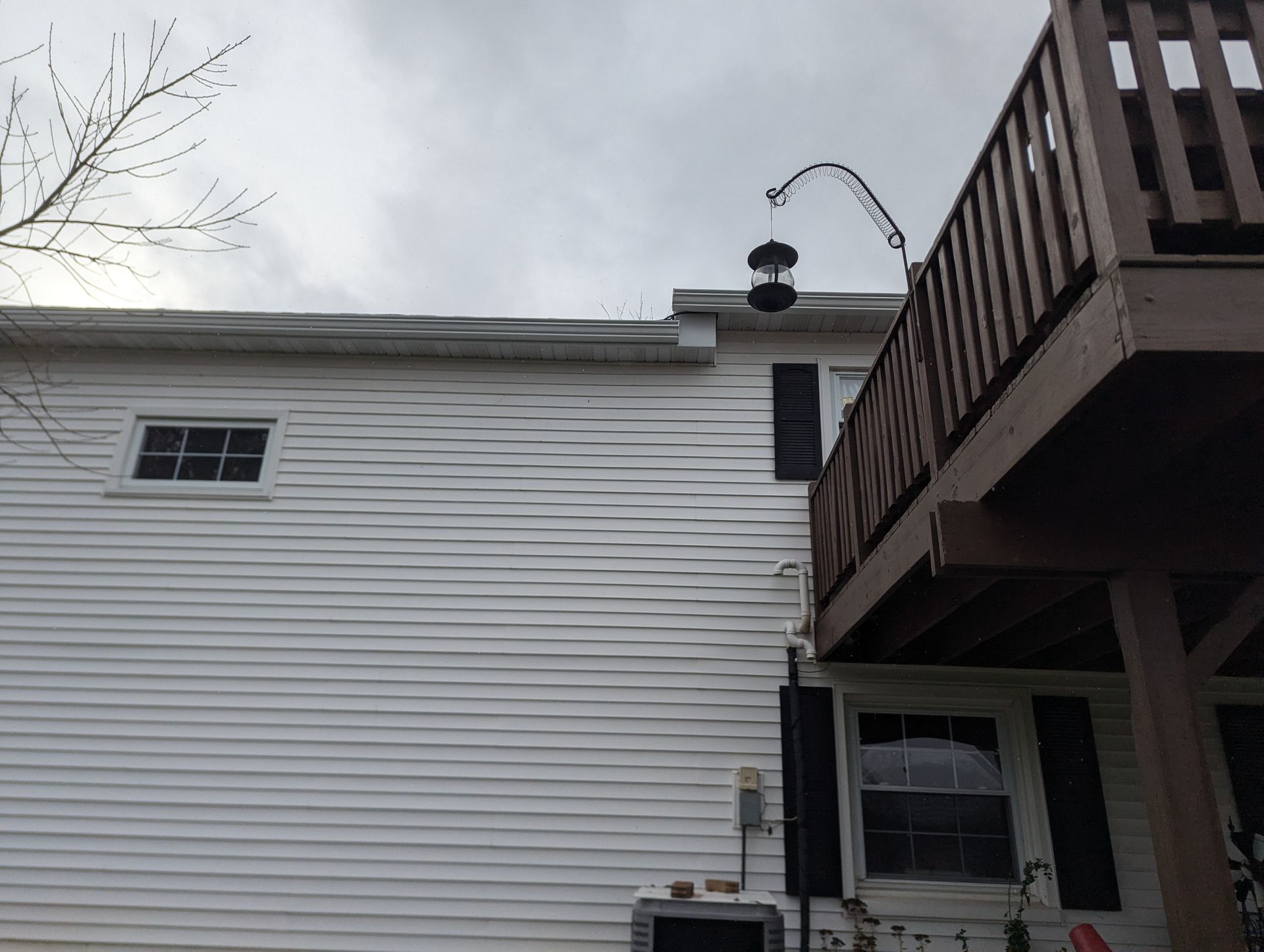 White house with siding, a dark wooden deck, and a bird feeder hanging from a curved metal arm. Cloudy sky.