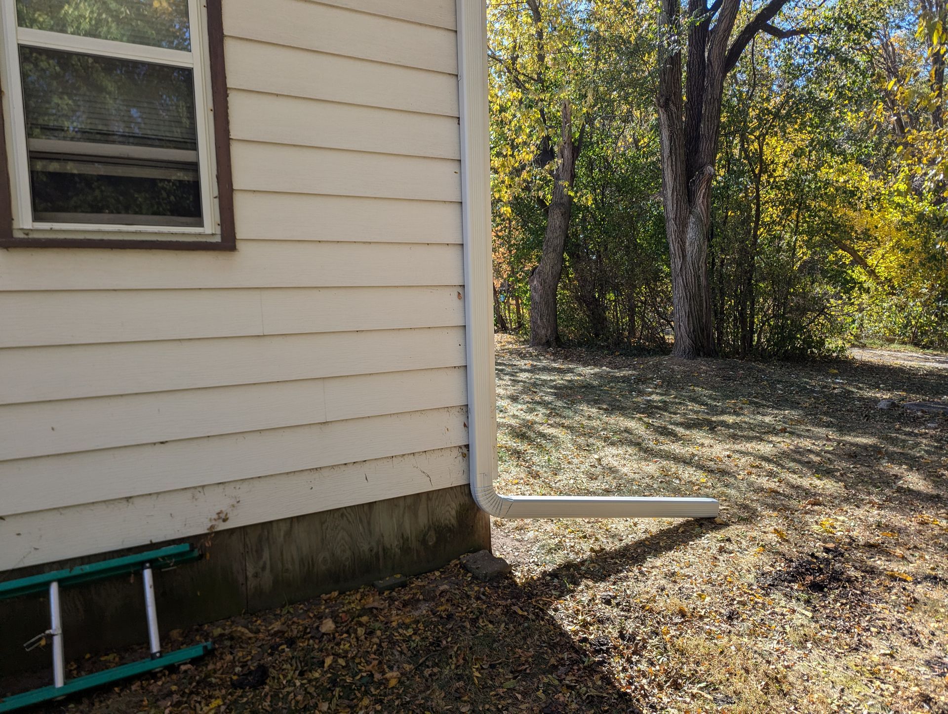 Corner of a house with a white gutter, window, and small ladder on a sunny day.