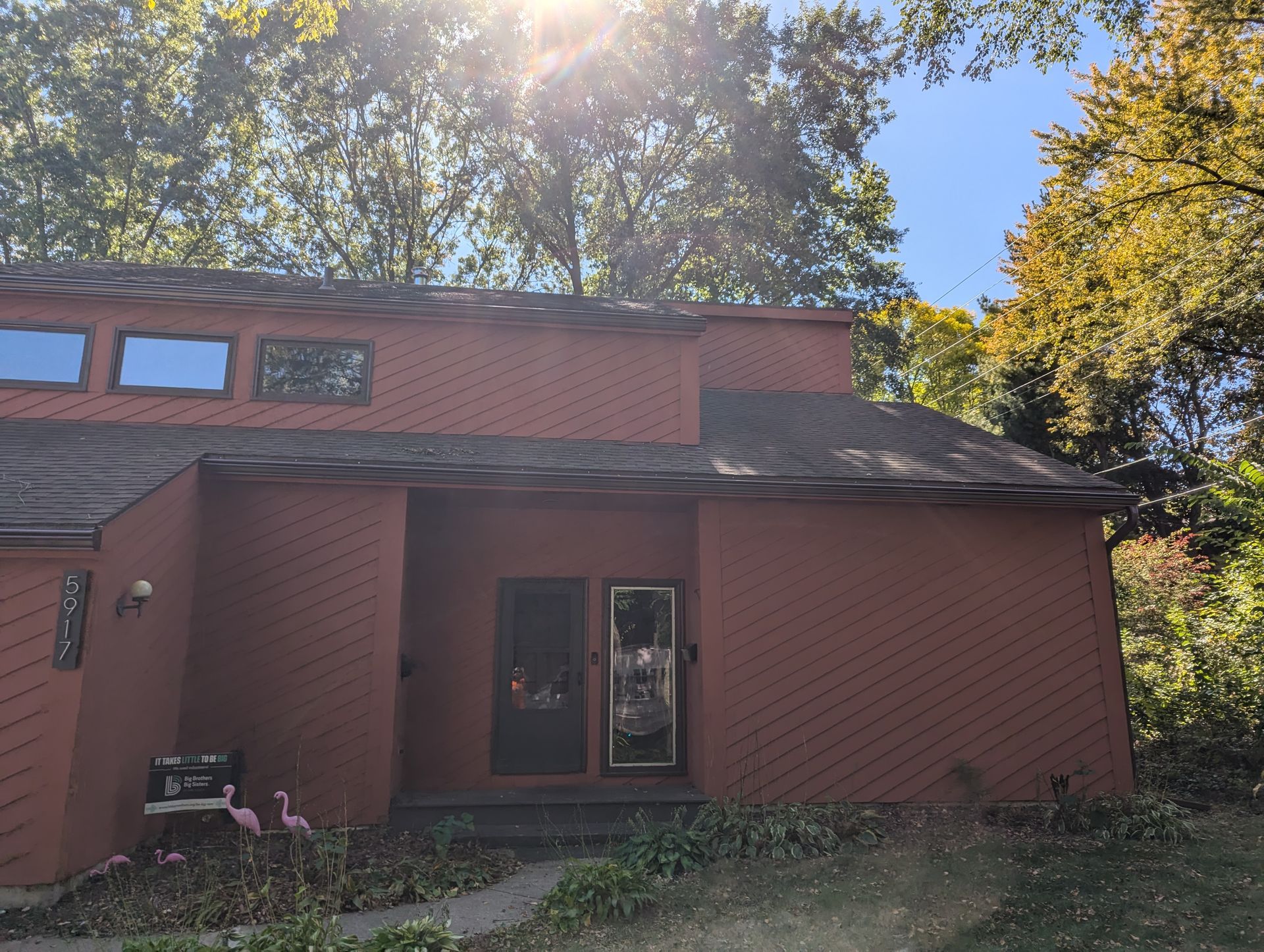 Red-sided house with a dark roof and two glass doors, surrounded by trees on a sunny day.