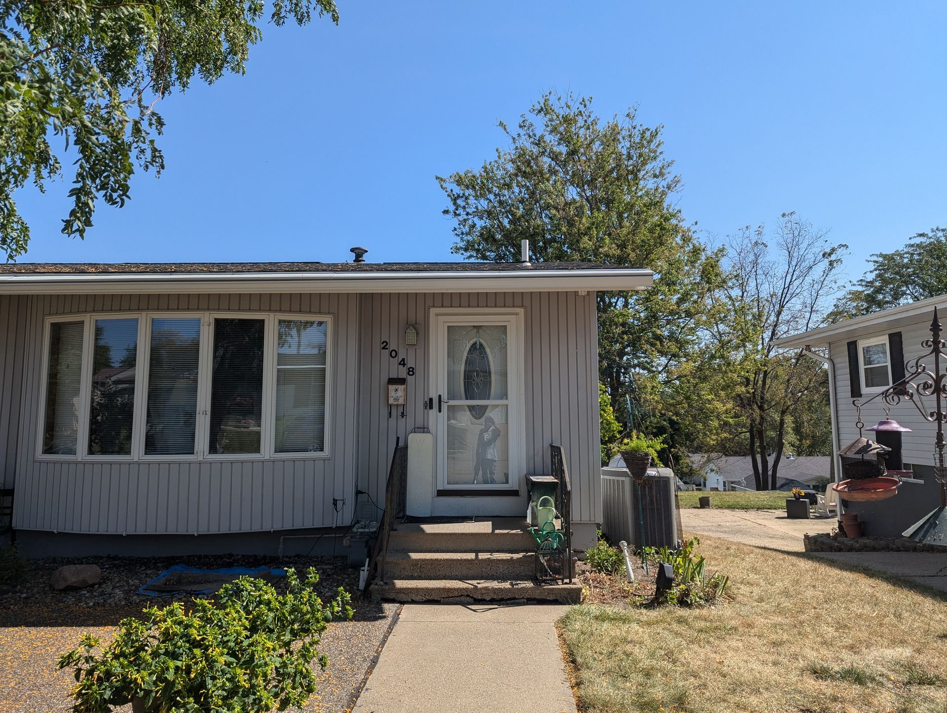 A gray house with a small front yard and a paved walkway under a clear blue sky.