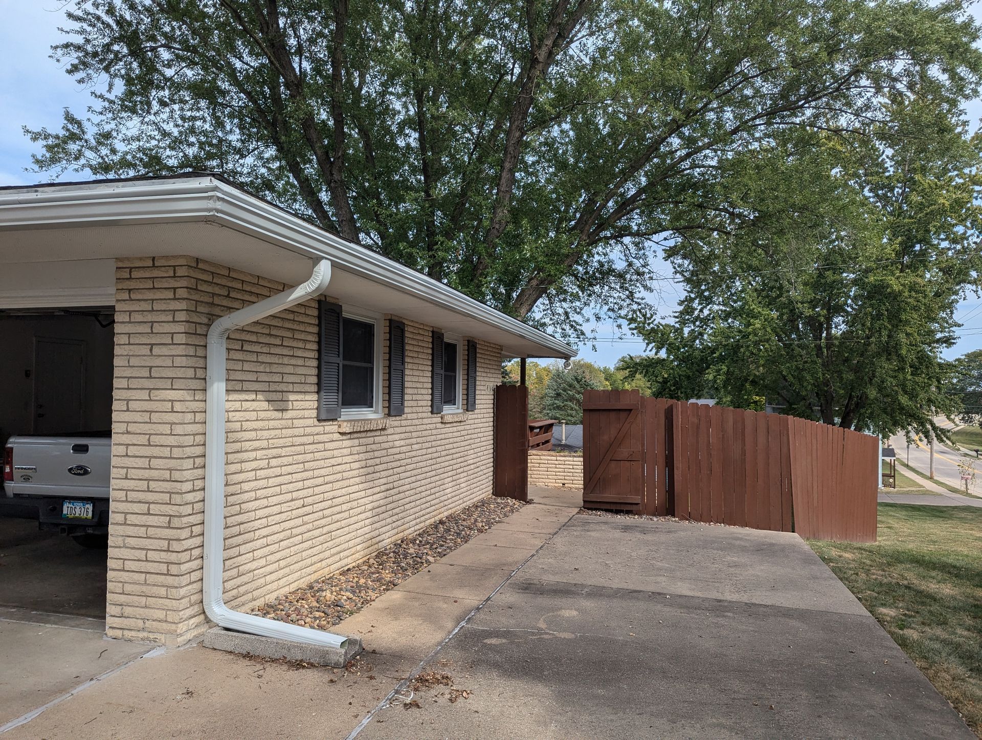Tan brick house with gray roof and a driveway, next to a brown wooden fence.