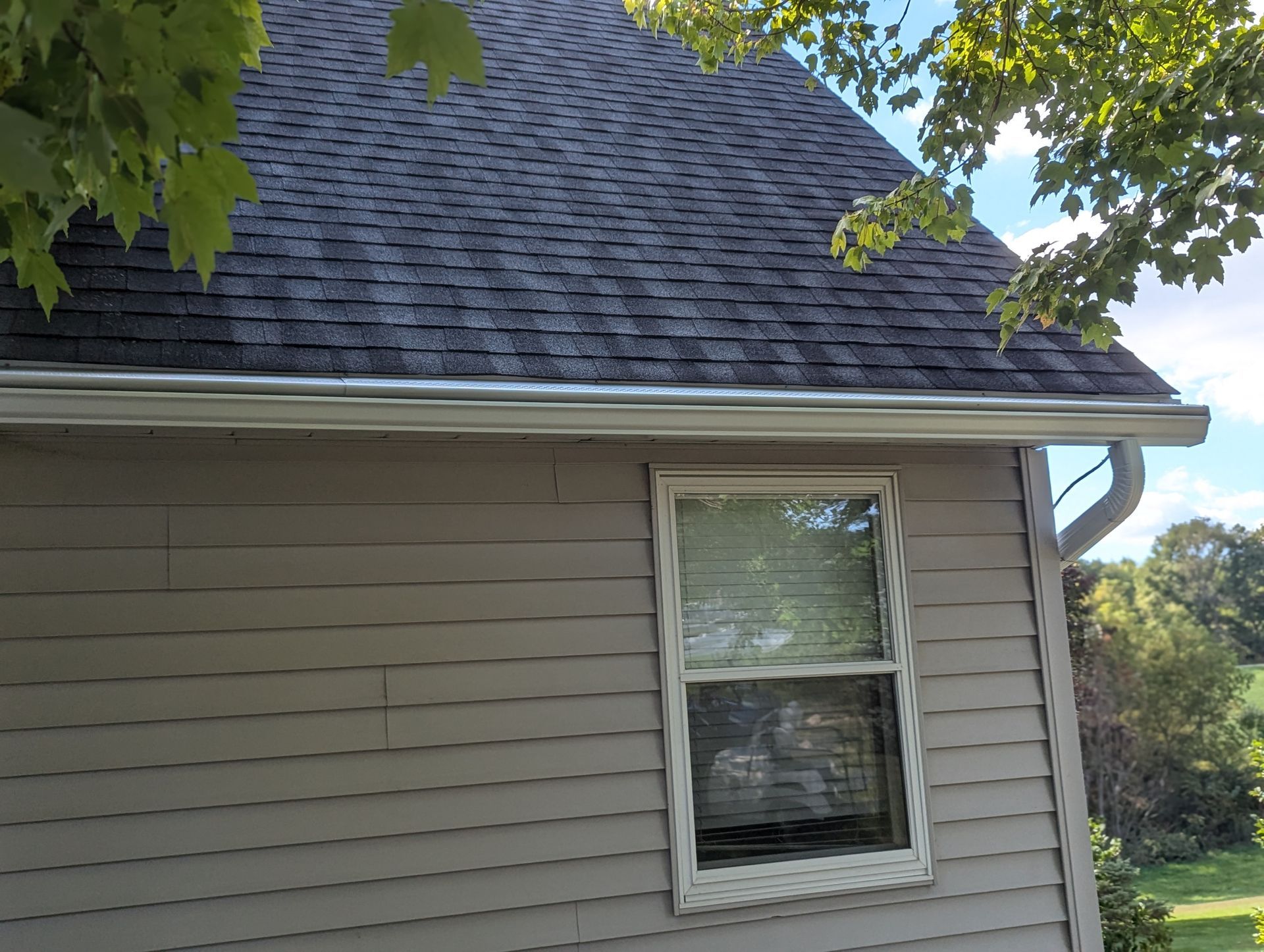 Gray house with dark gray shingle roof and white gutters. Window is centered below the roof.