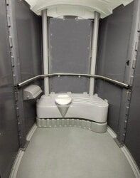 Interior of a portable toilet; gray walls, toilet, and handrail, for disabled access.