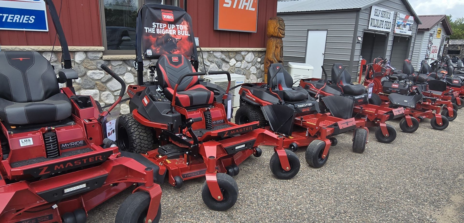 Row of red and black lawn mowers lined up outside a shop