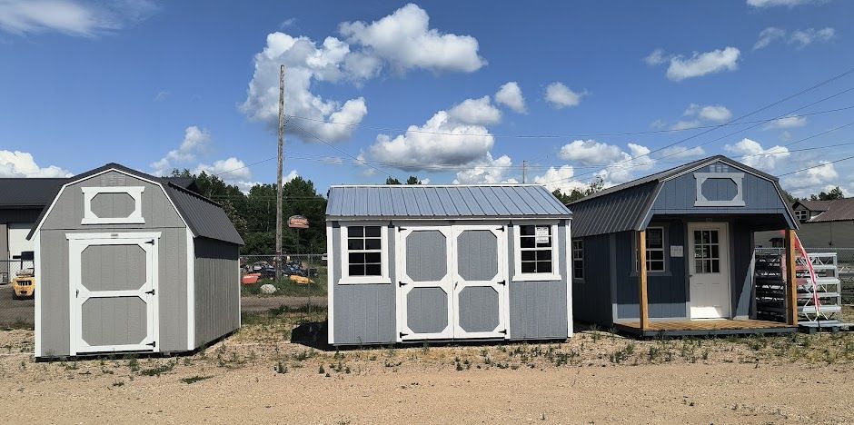 Three small gray and white sheds outdoors under a blue sky with clouds