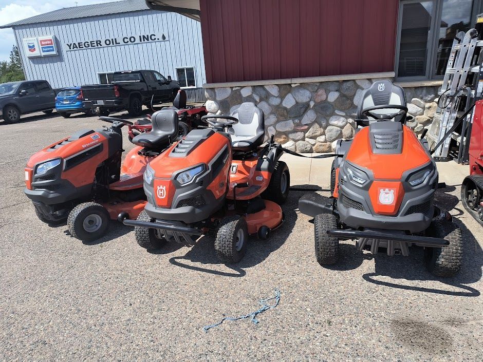 Three orange riding lawn mowers parked outside a building on a gravel lot.