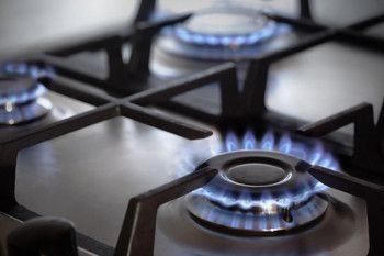 Close-up of gas stove burners with blue flames on a stainless steel cooktop