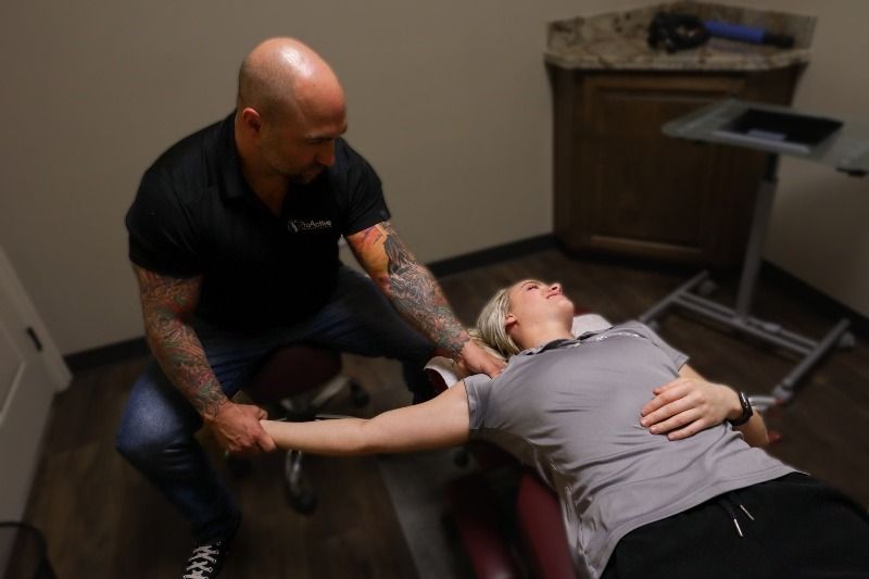 Chiropractor adjusting woman's shoulder in a treatment room.