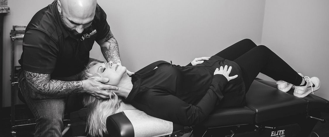 A chiropractor adjusting a woman's neck; she lies on a table, looking upwards.