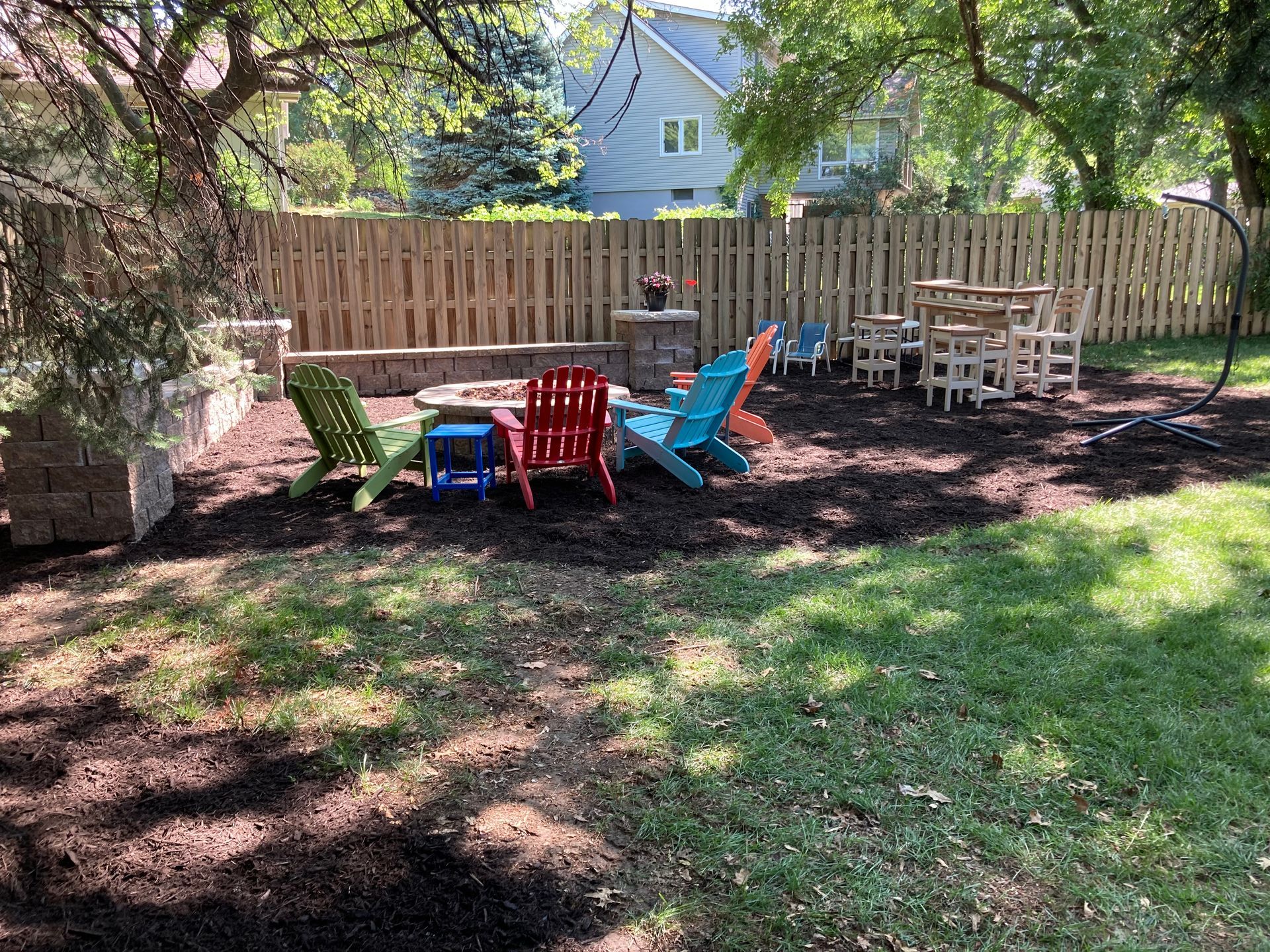 a group of colorful chairs are sitting in a backyard next to a wooden fence
