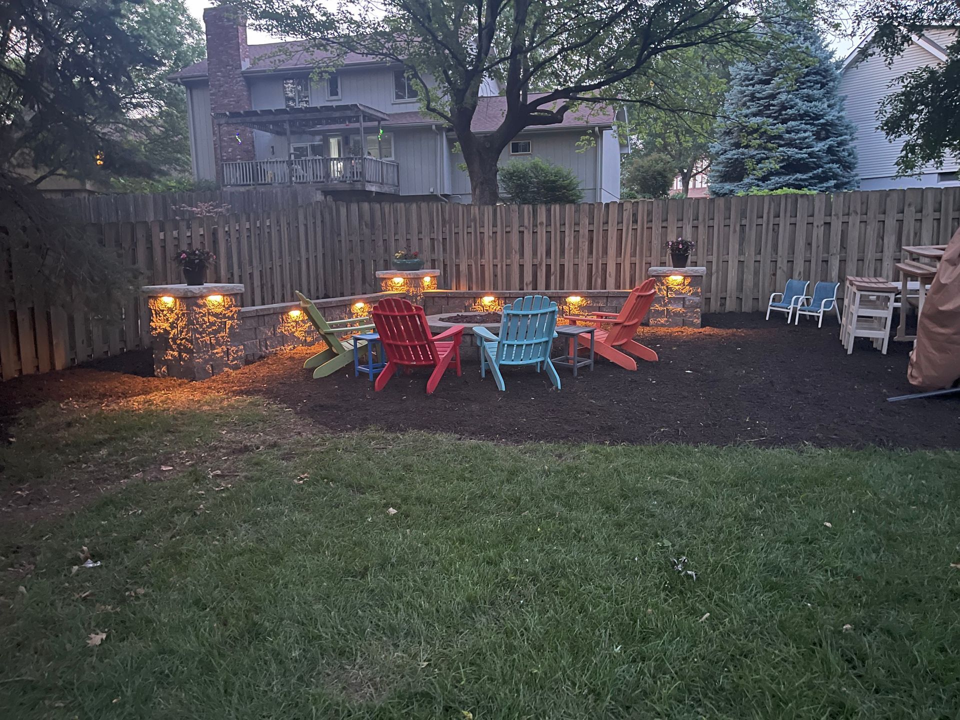 a group of colorful chairs are sitting around a fire pit in a backyard