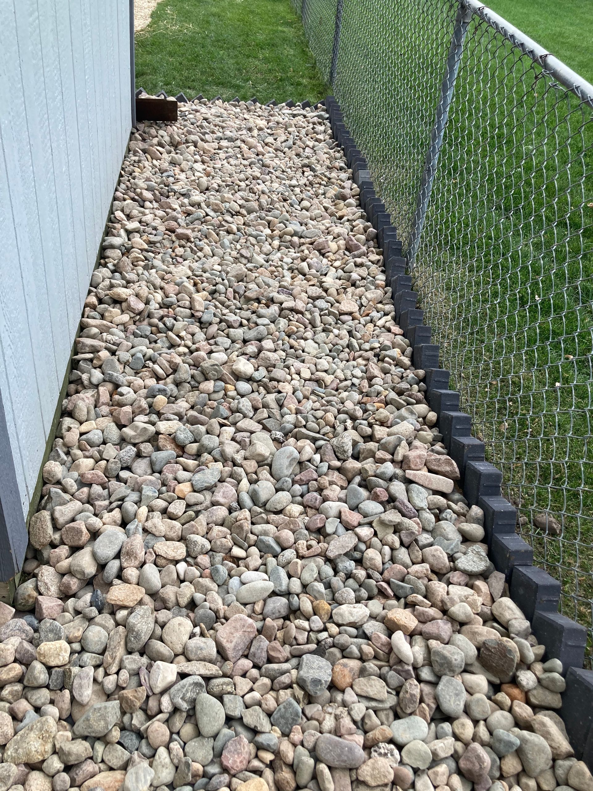 a walkway filled with rocks next to a chain link fence