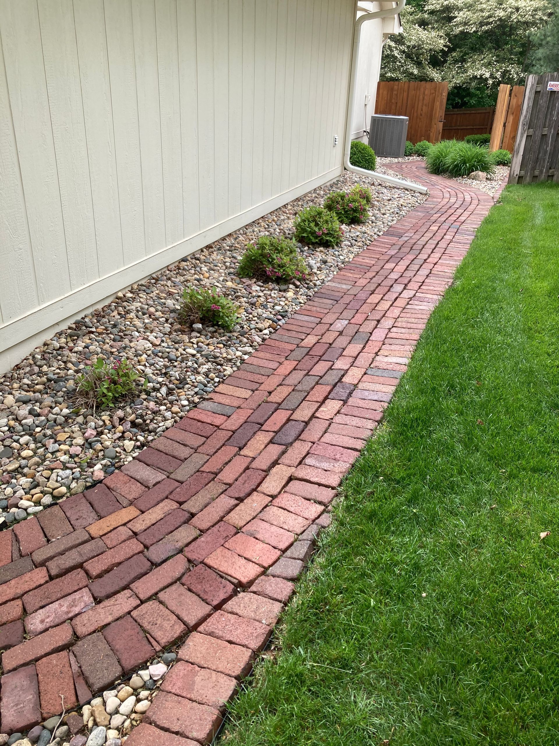 a brick walkway leading to a house next to a fence