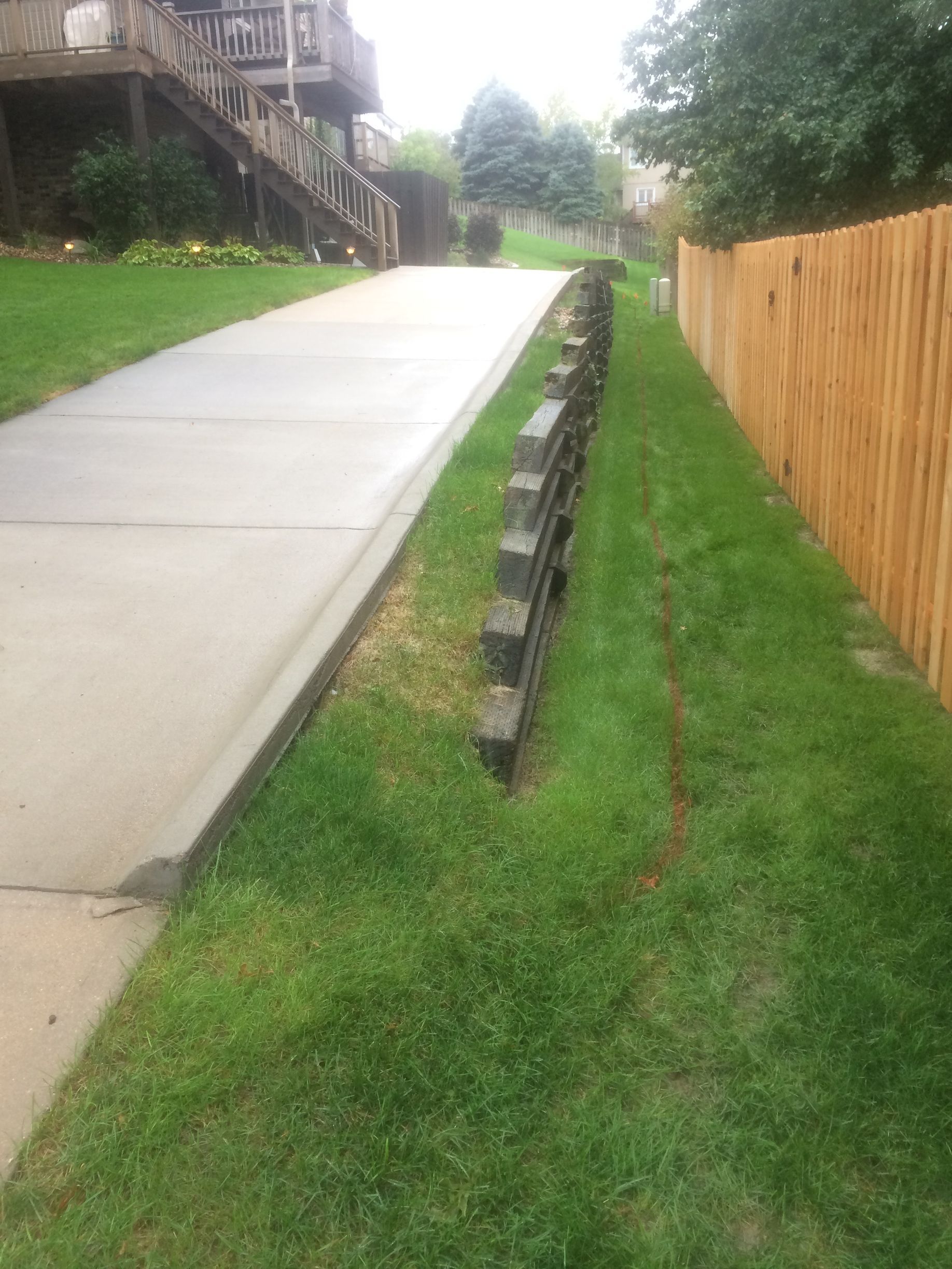 a concrete driveway leading to a house with a wooden fence