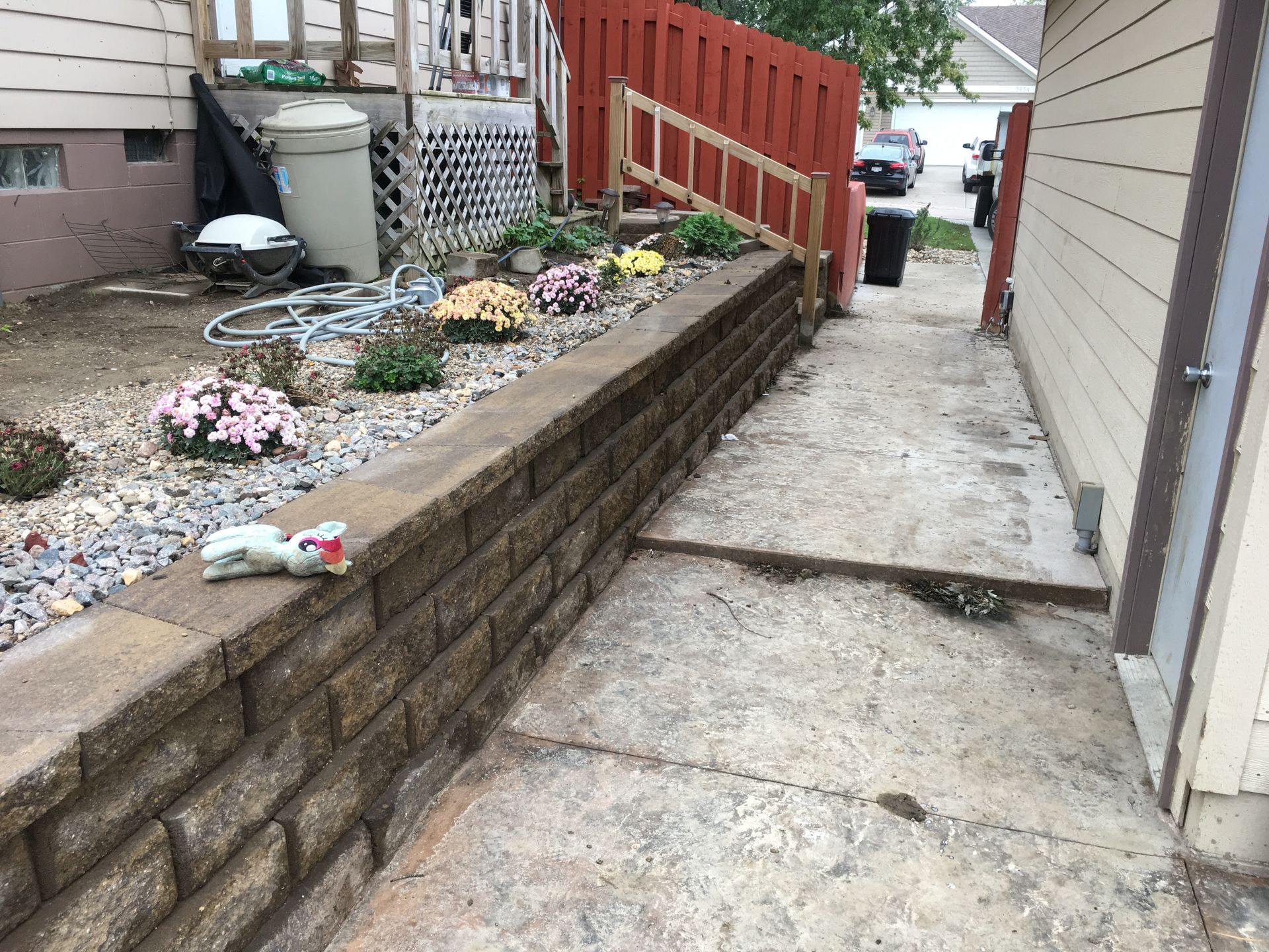 a brick wall is surrounded by flowers and rocks in front of a house
